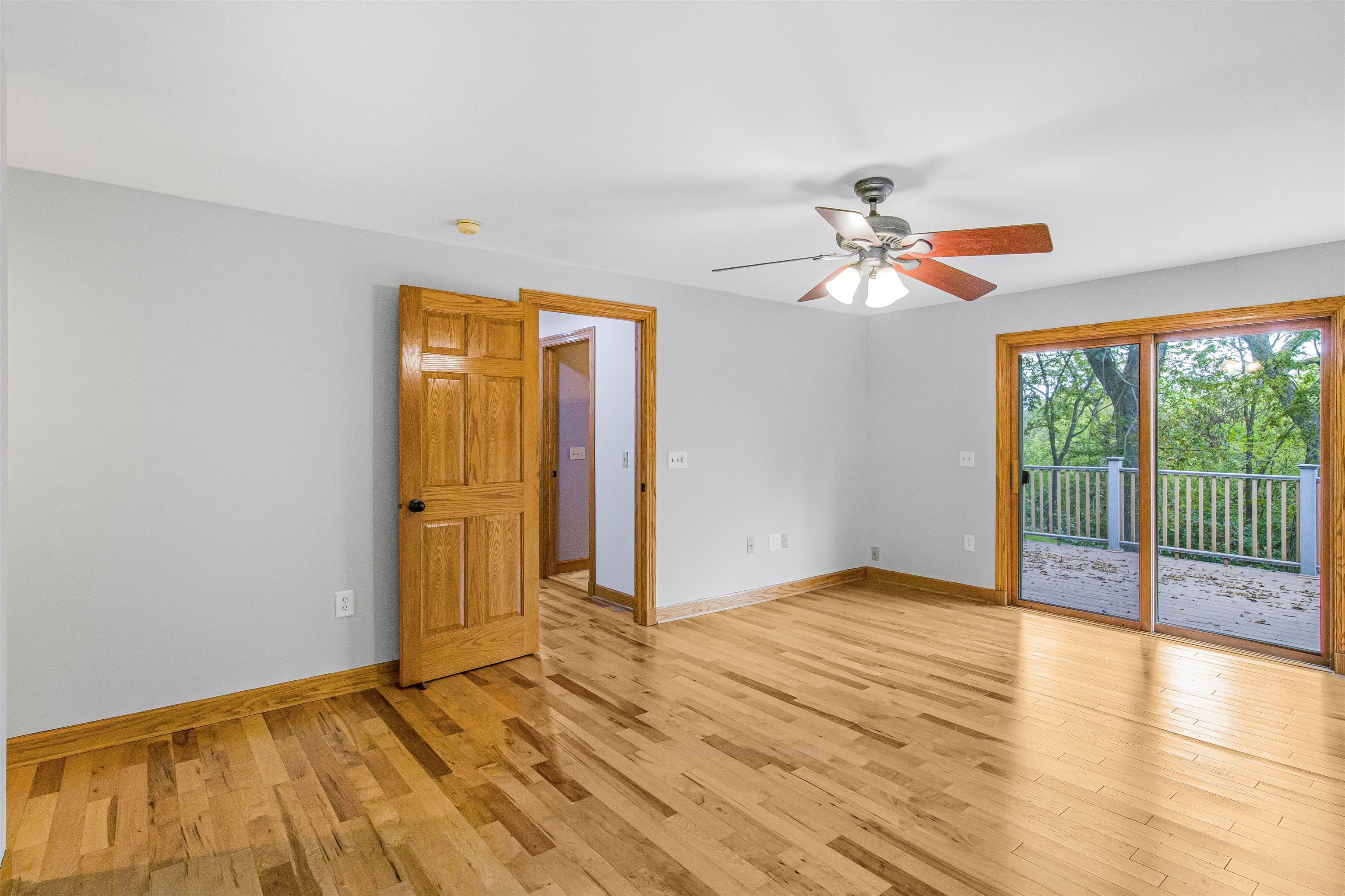 Empty room with hardwood floors, a ceiling fan, and sliding glass doors to a deck.