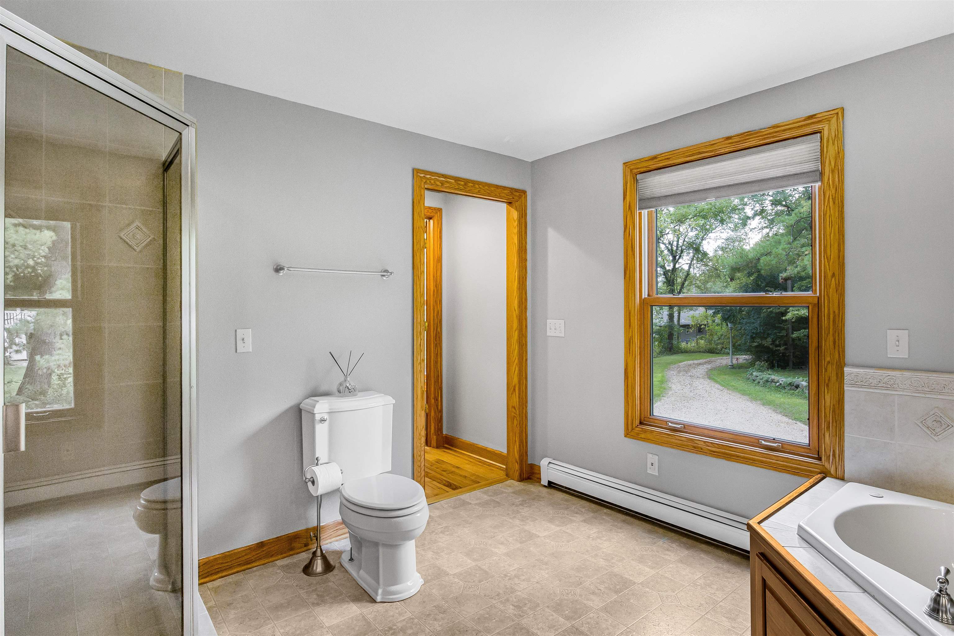 Bathroom with glass shower, corner soaking tub, and a large window overlooking a green yard.