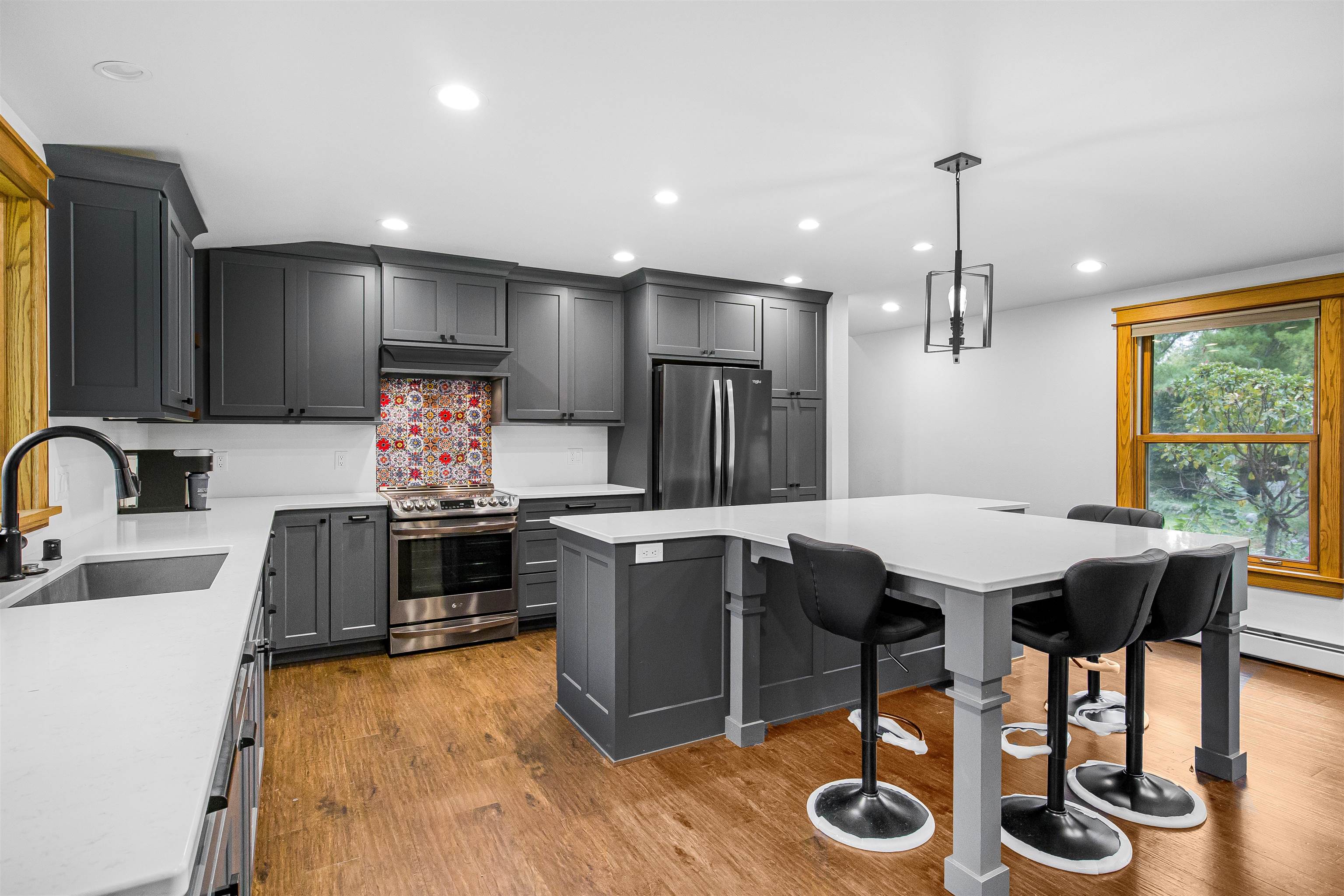 Kitchen with charcoal cabinets, stainless steel appliances, patterned backsplash, and a large island with stools.