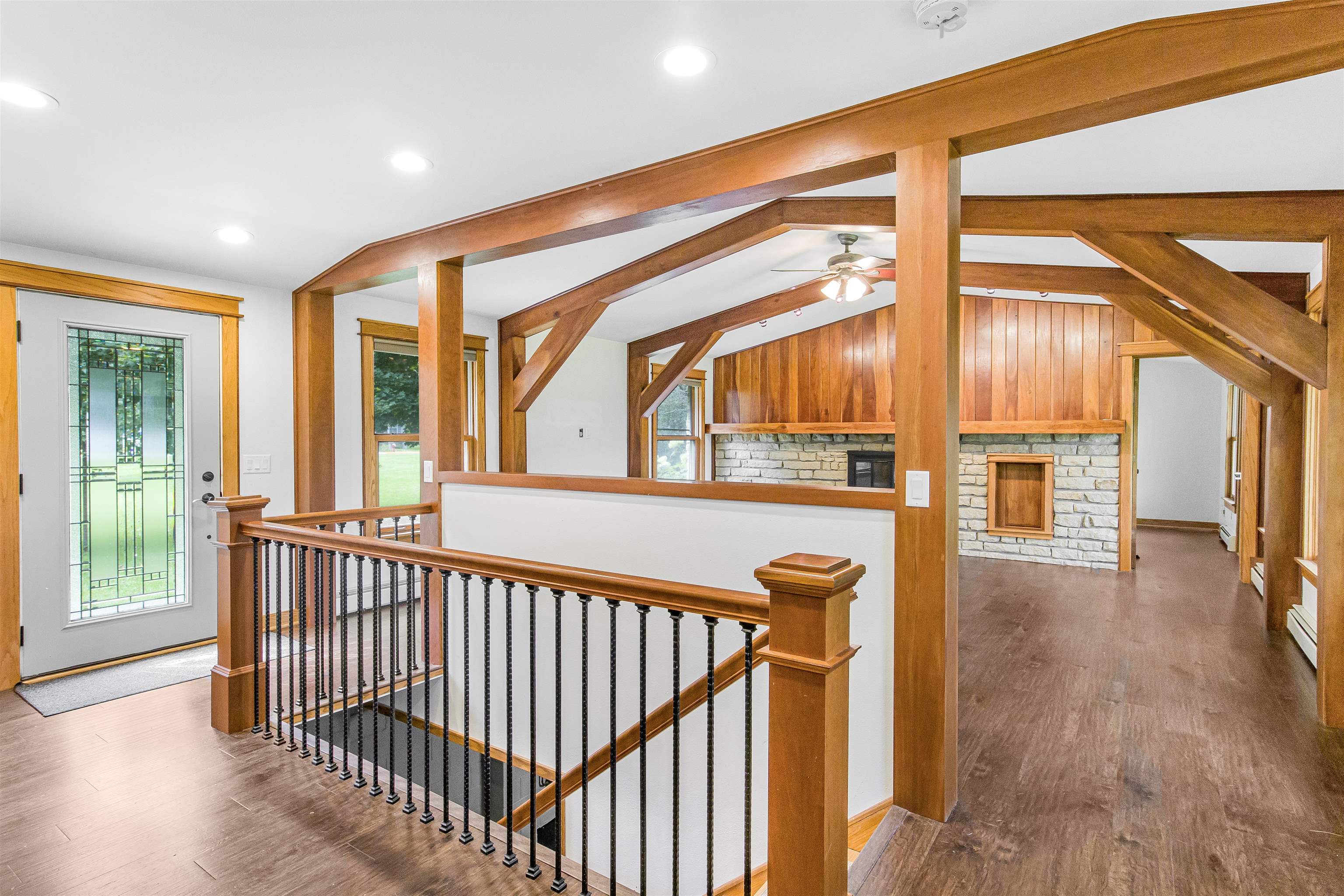 Entry hall with timber beams, a stairway railing, and a stone fireplace in the adjoining room.