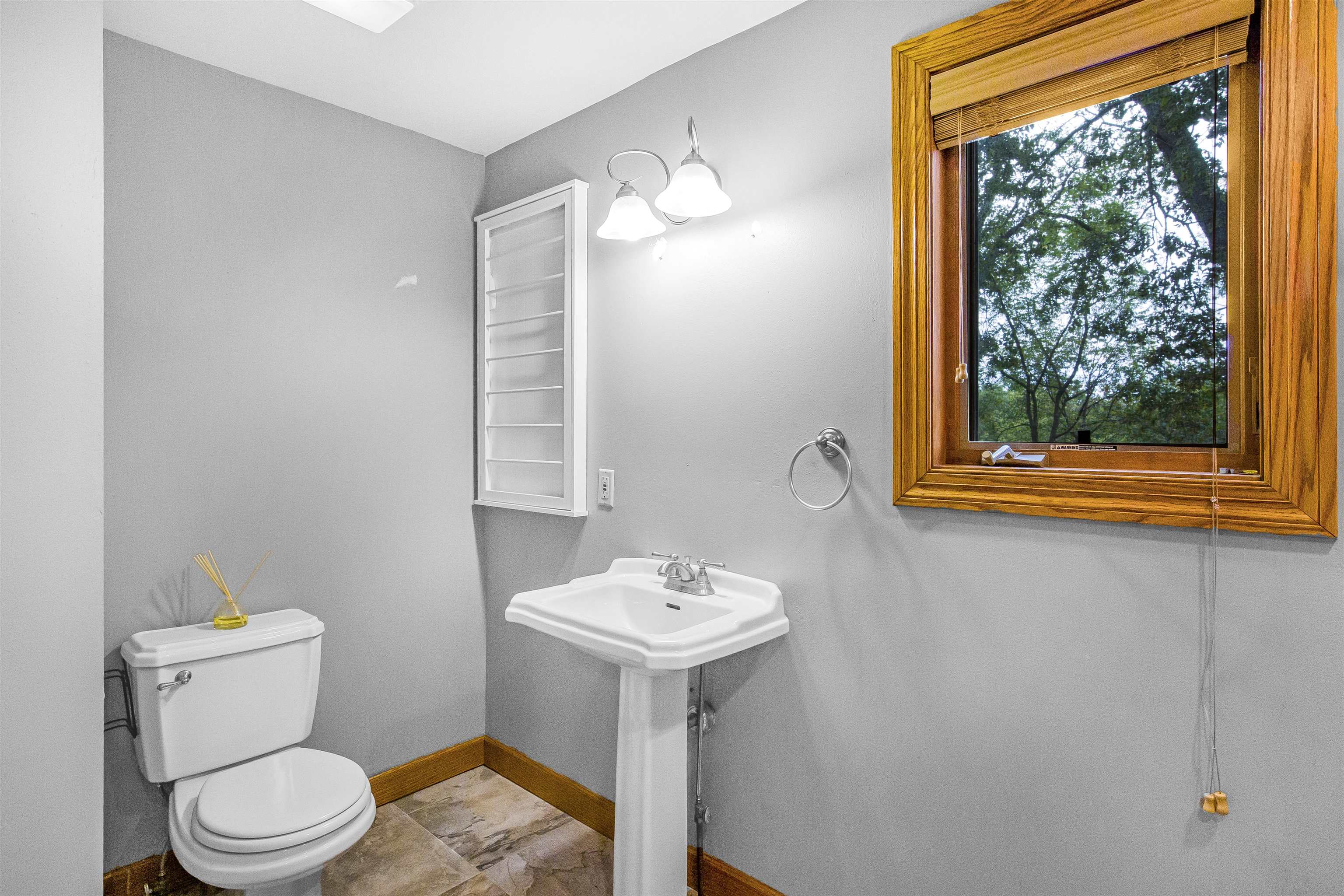 Bathroom with a white pedestal sink and toilet beside a large wood-trimmed window.