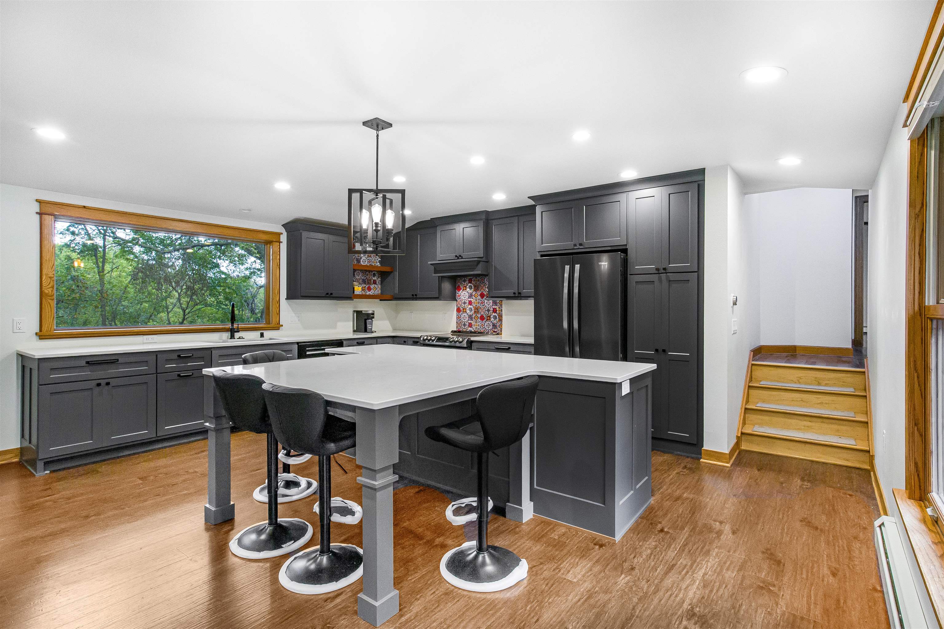 Modern kitchen with charcoal cabinets, a large island, and a wide window overlooking trees.