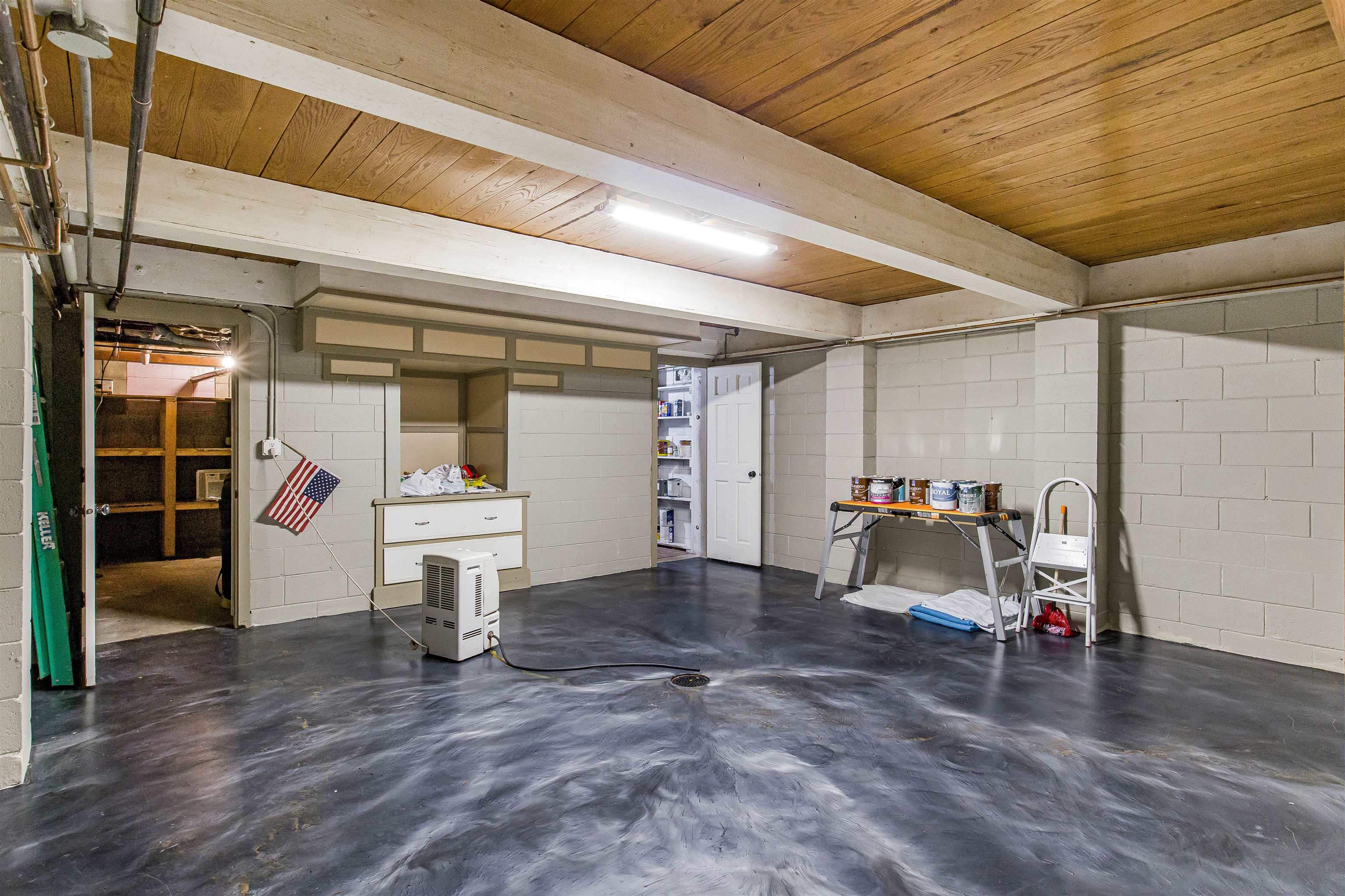 Basement with polished concrete flooring, cinder-block walls, and exposed beams beneath a wood-plank ceiling.