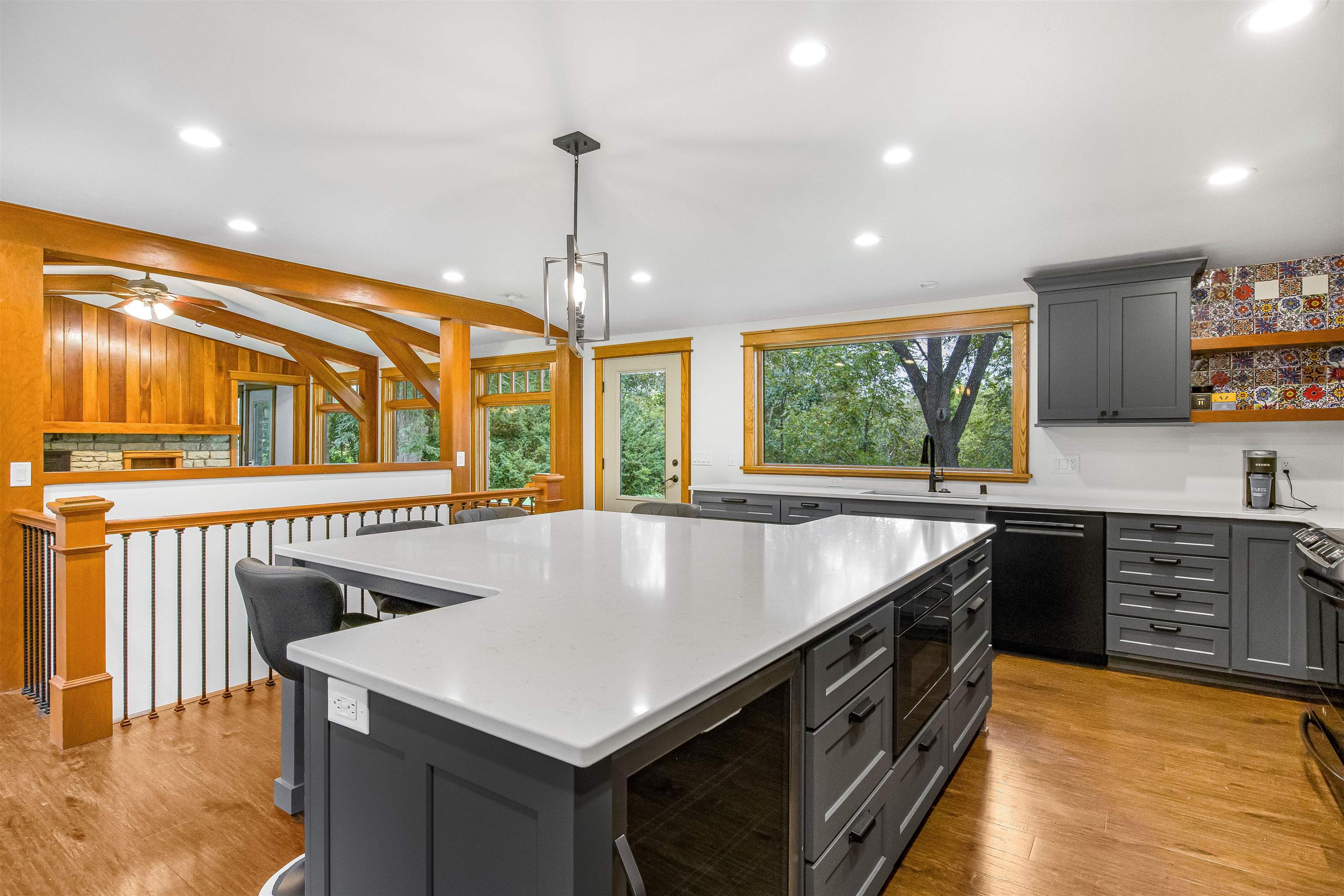 Kitchen with a large white-countertop island, charcoal cabinets, patterned tile backsplash, and warm wood beams.