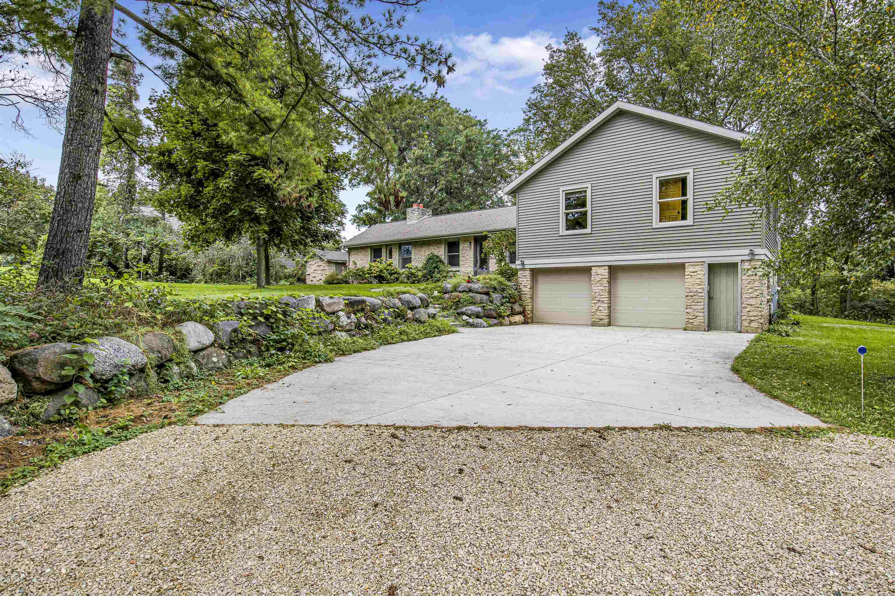 House exterior with a broad driveway, two garage doors, and a landscaped stone retaining wall.