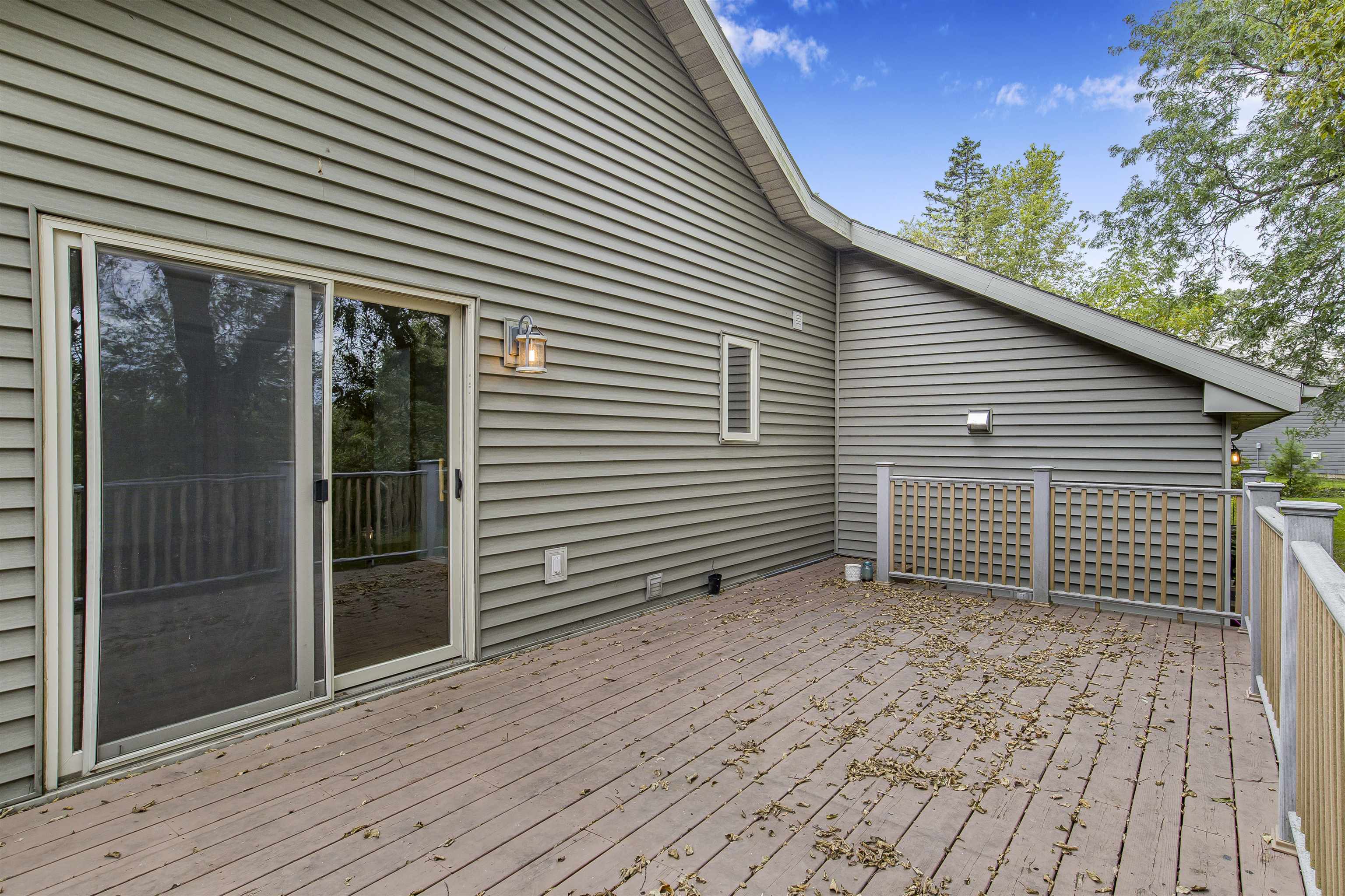 Raised wooden deck with gray siding, sliding glass door, and autumn leaves scattered across the boards.
