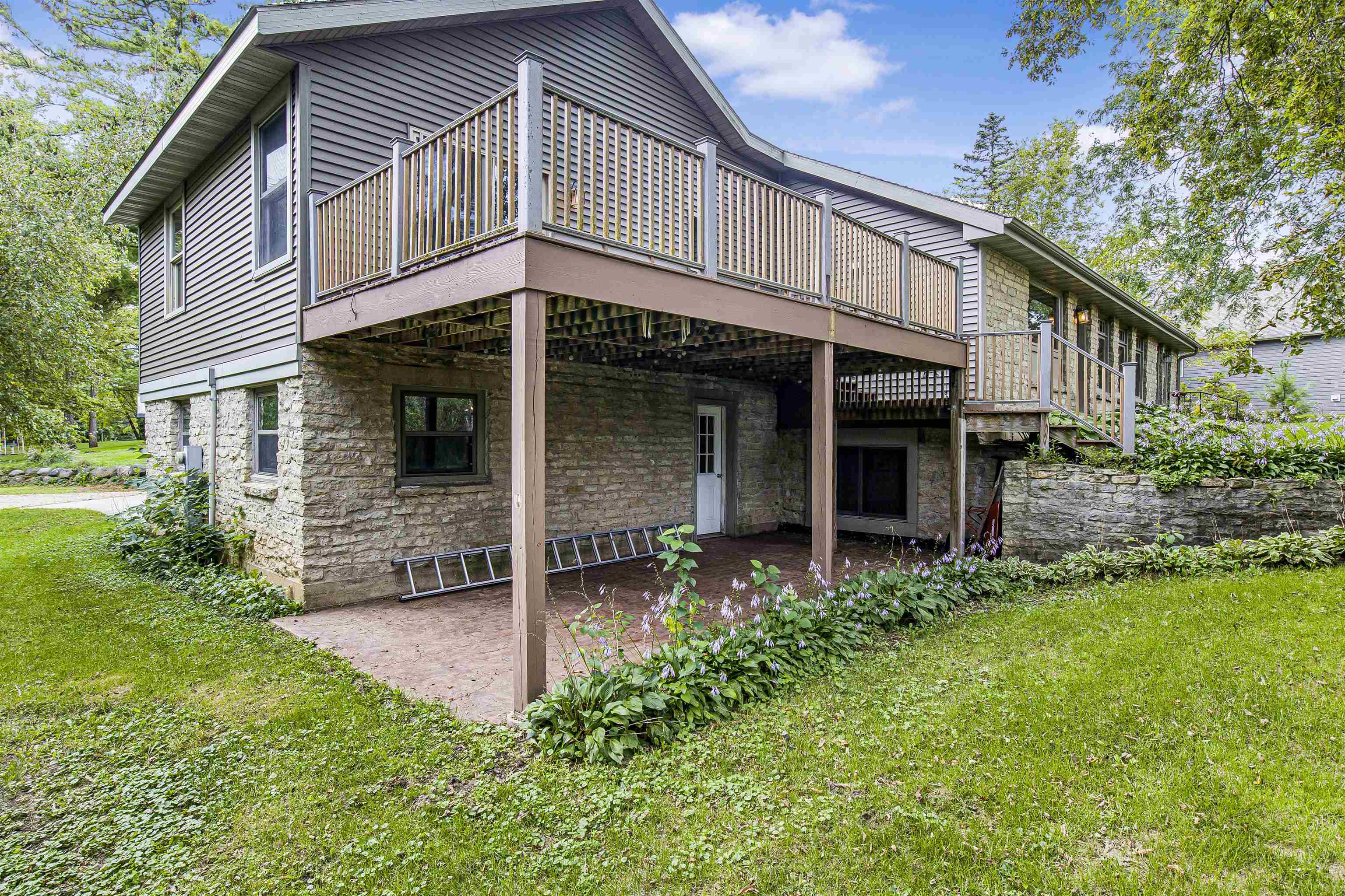 Home rear exterior with an elevated wooden deck, stone lower level, and covered patio.