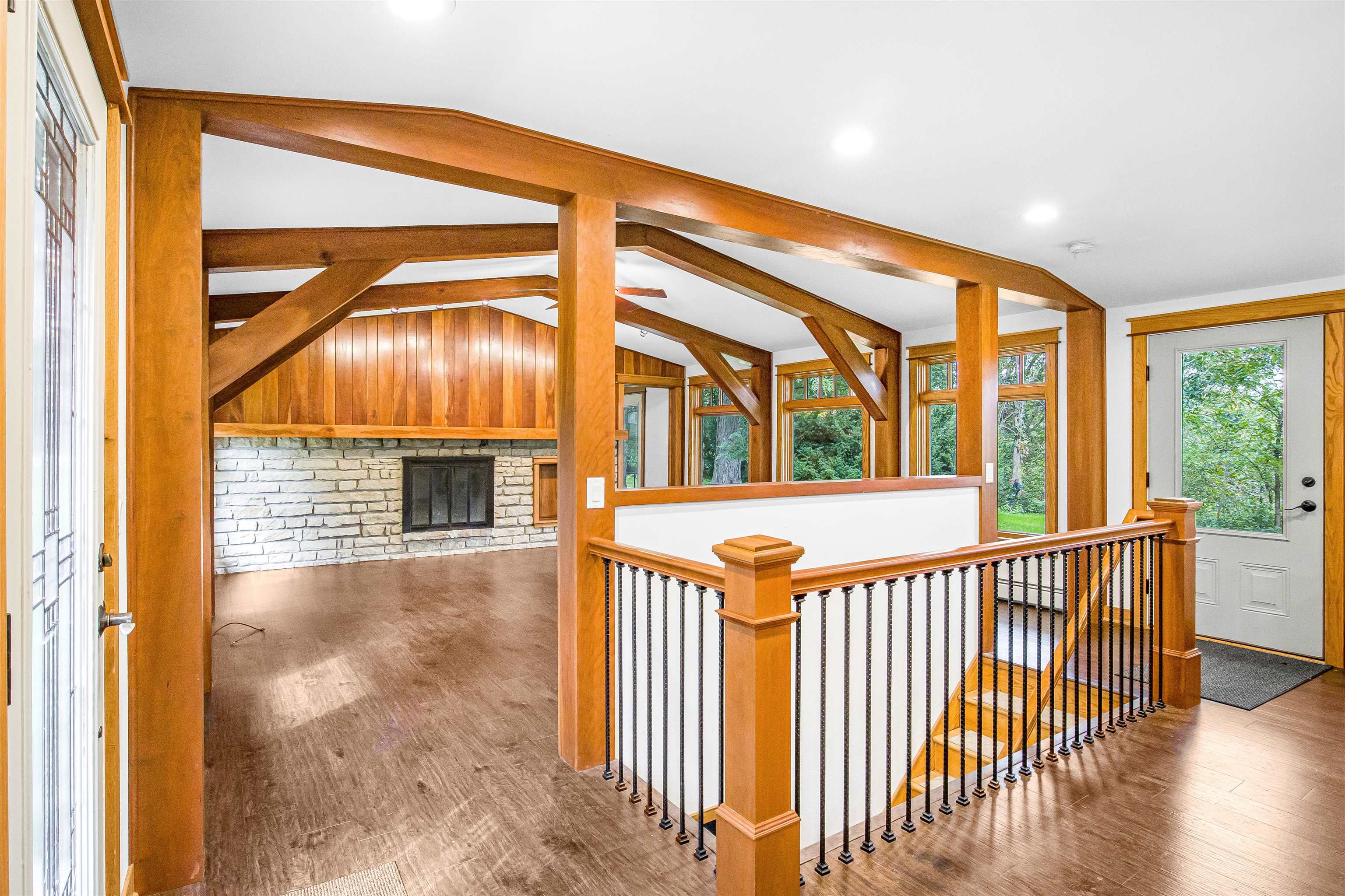Open living room with a stone fireplace, exposed timber beams, and a wood-and-iron stair railing.