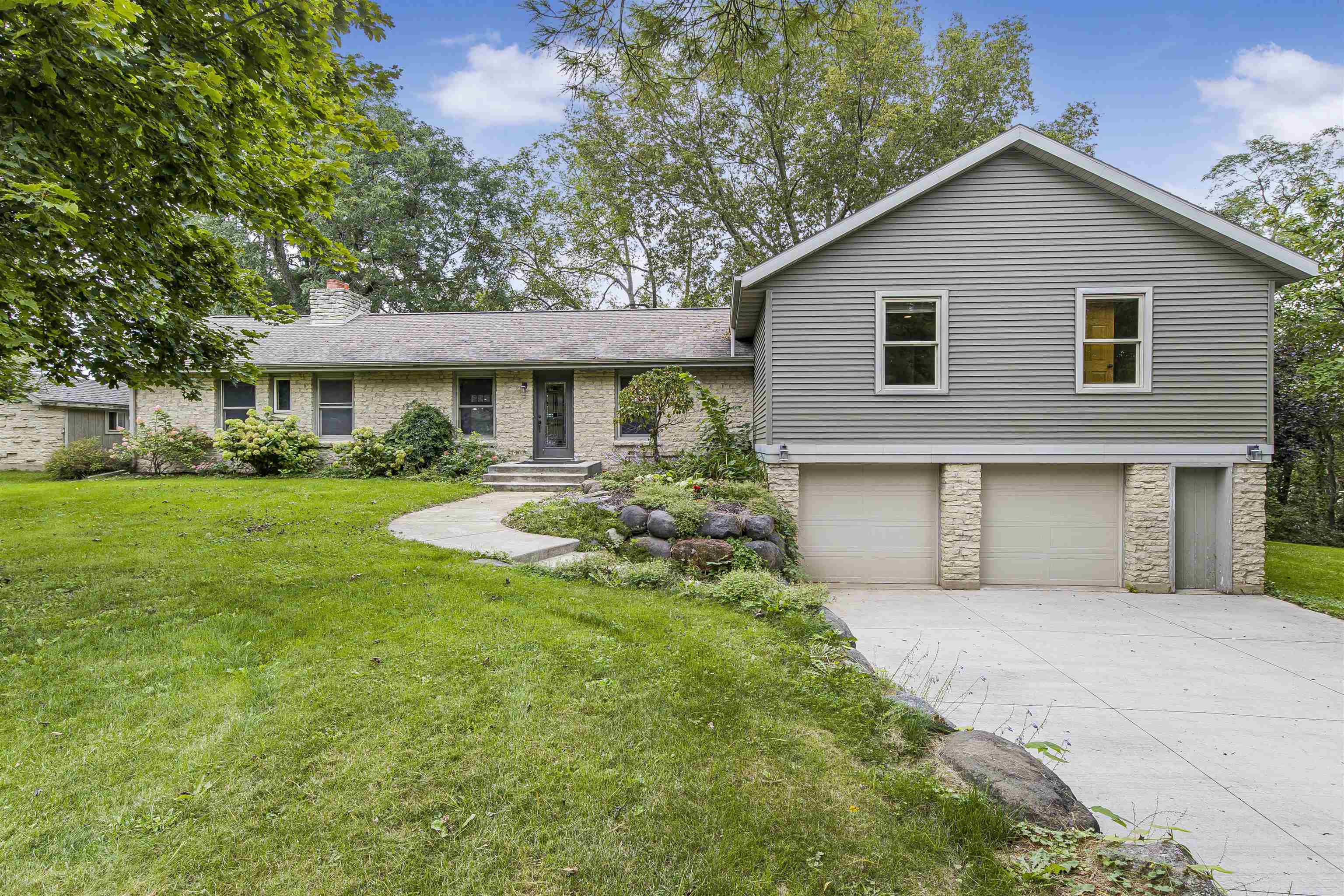 Stone-and-gray-sided home with a raised two-car garage, curved walkway, and landscaped front lawn.
