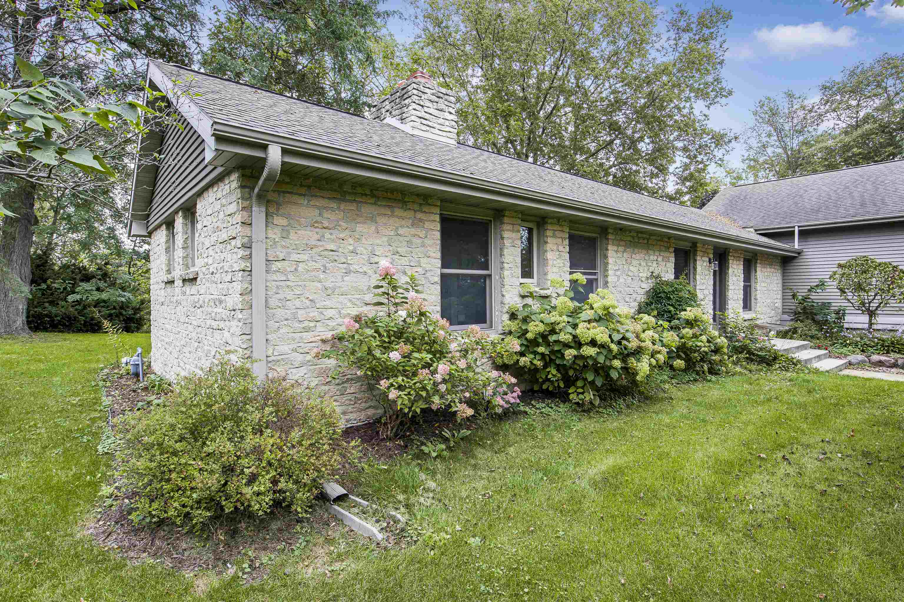 Stone house exterior with a prominent chimney and flowering shrubs along the lawn.