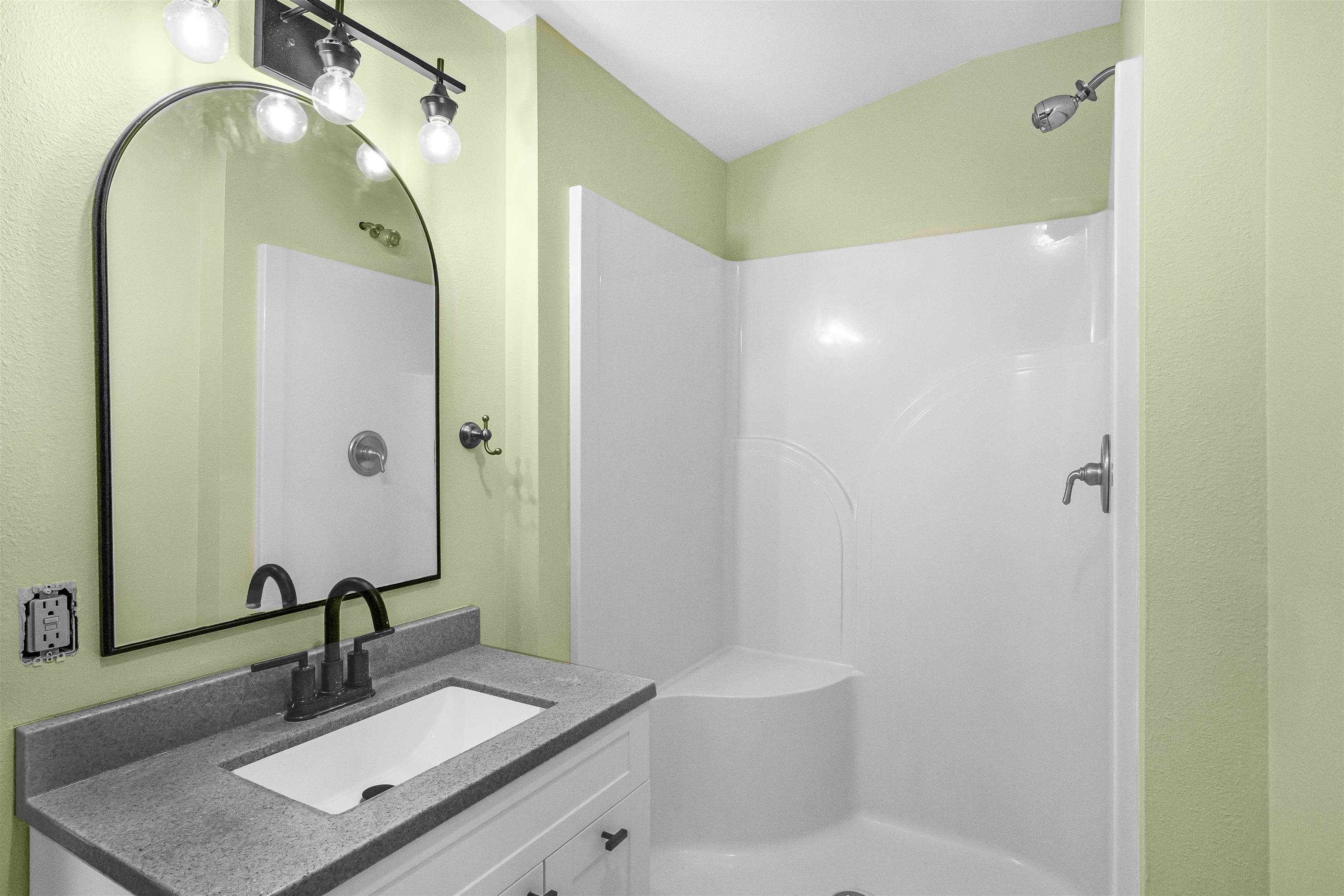 Bathroom with a white shower, gray vanity countertop, black faucet, and large arched mirror.
