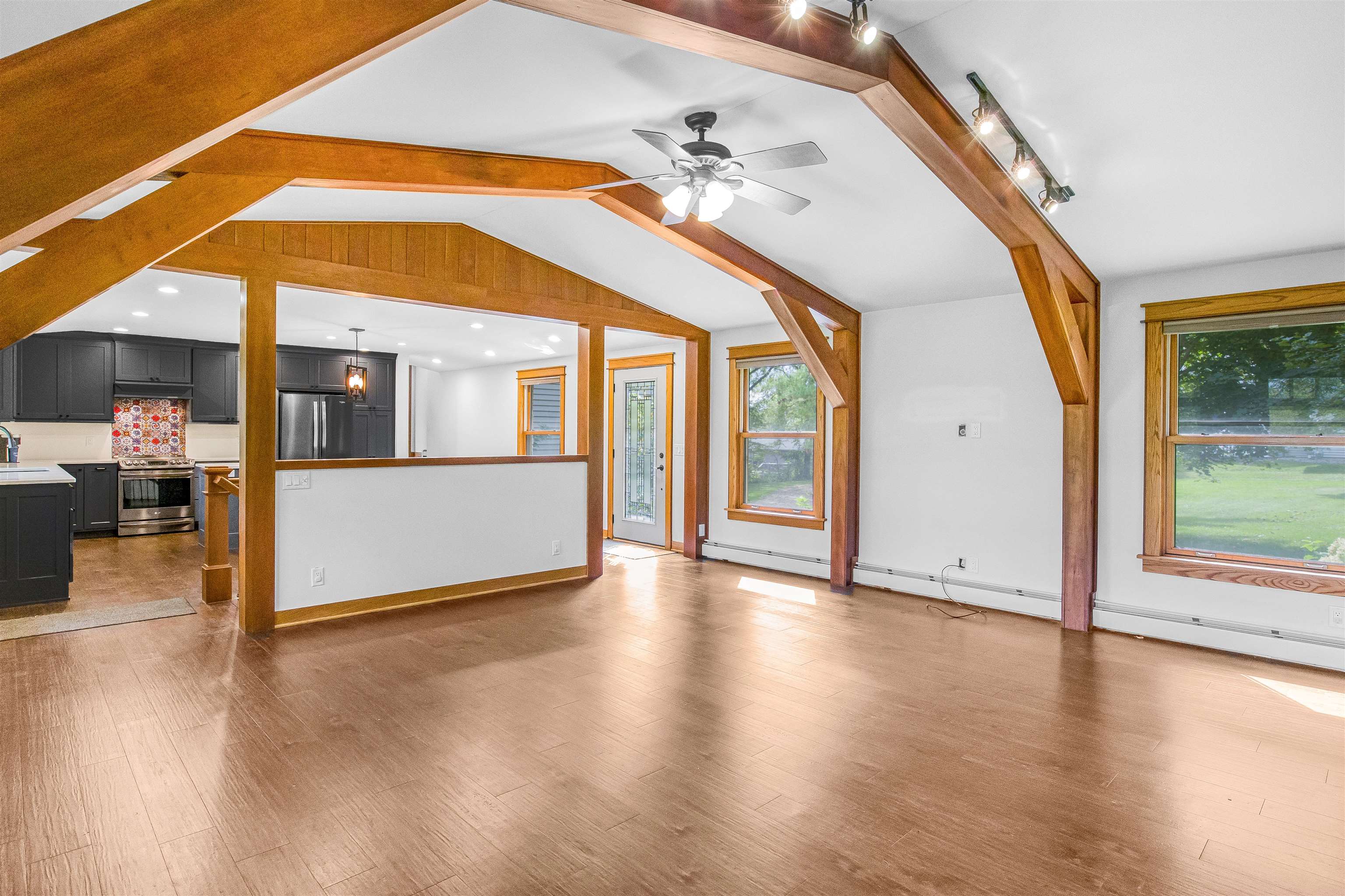 Vacant living room with exposed timber ceiling beams, wood-look floors, and an open kitchen.