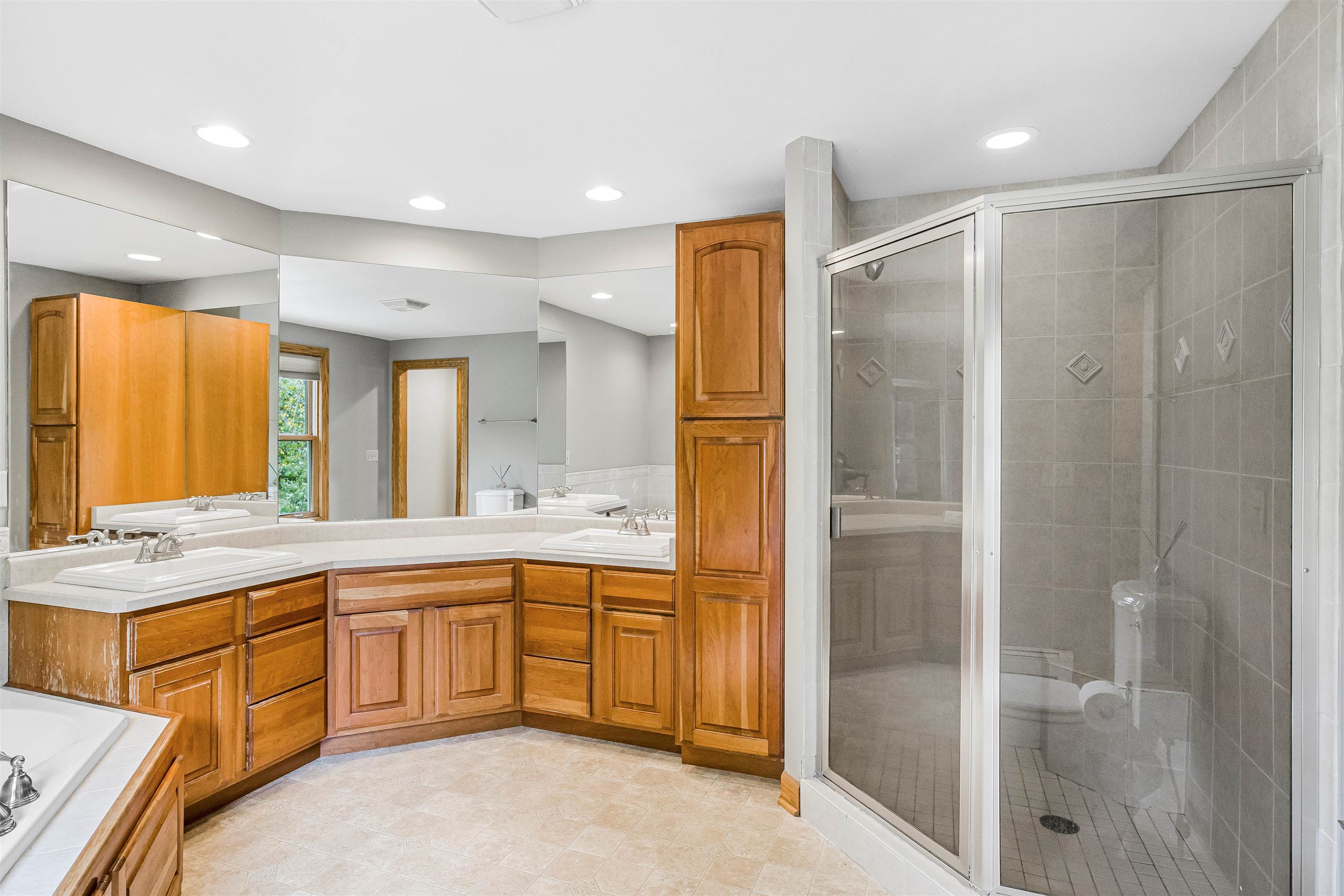 Bathroom with warm wood cabinetry, double sinks, large mirrors, and a glass-enclosed tiled shower.