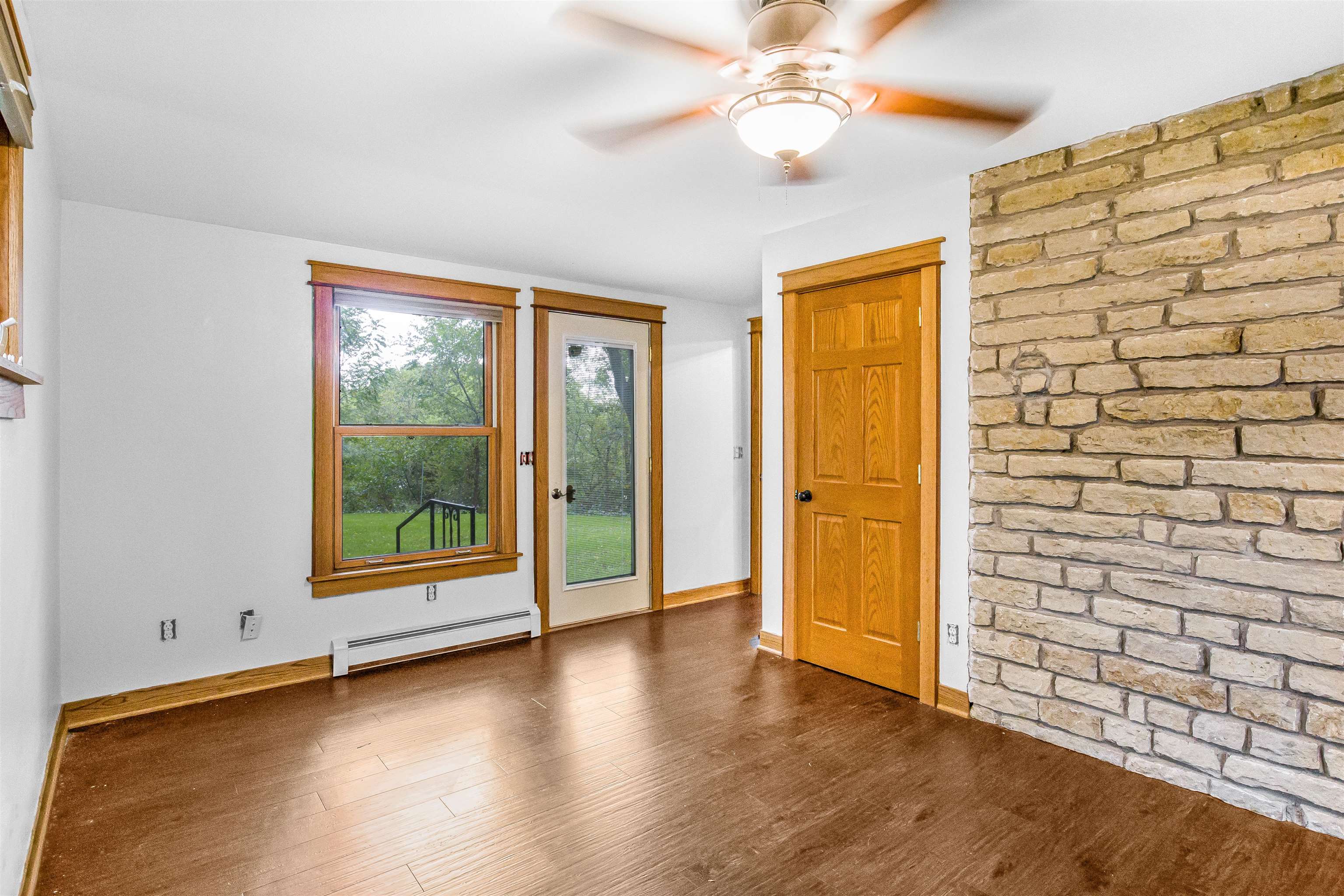 Vacant room with wood floors, a large window, and a stone accent wall.
