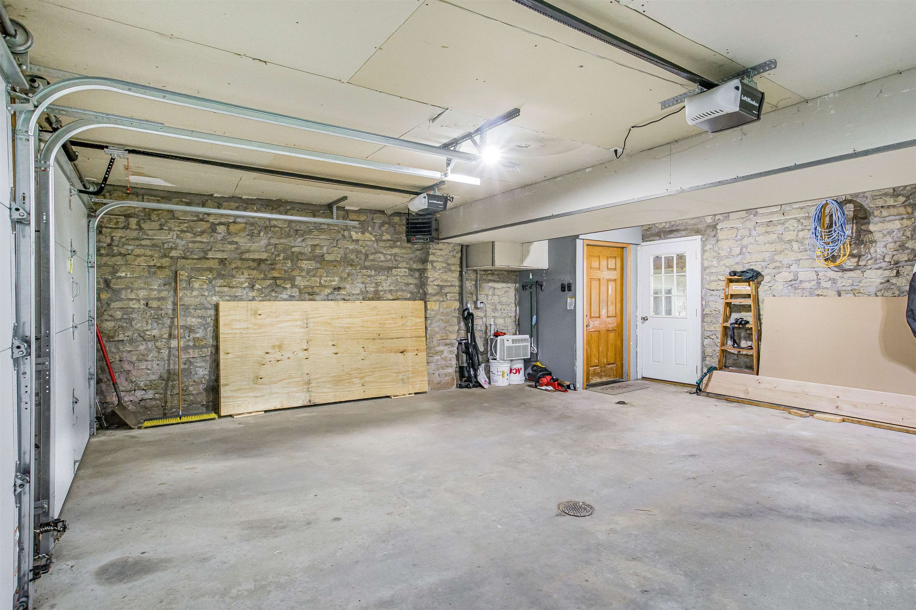 Spacious garage with exposed stone walls, overhead door tracks, and boards and tools along the walls.
