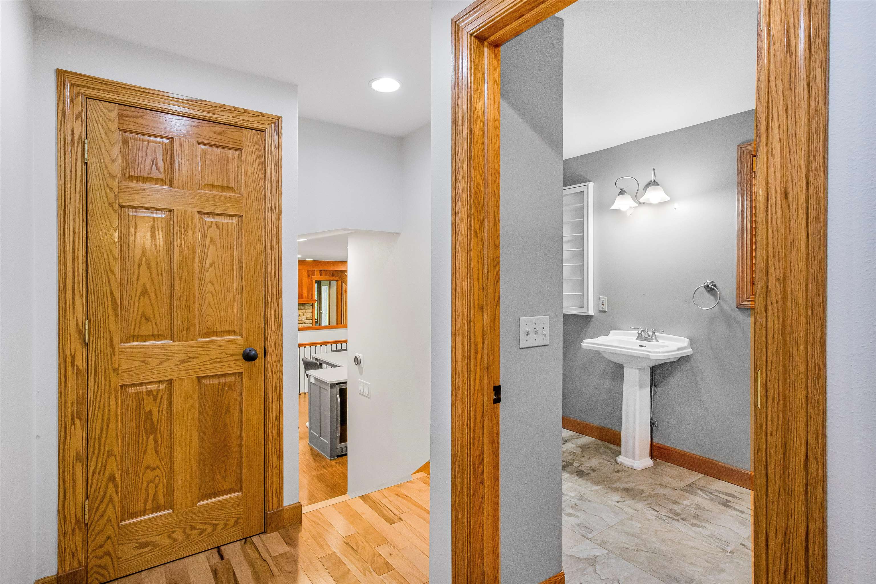 Bathroom with a white pedestal sink, gray walls, and patterned tile flooring, viewed through oak-trimmed doorways.