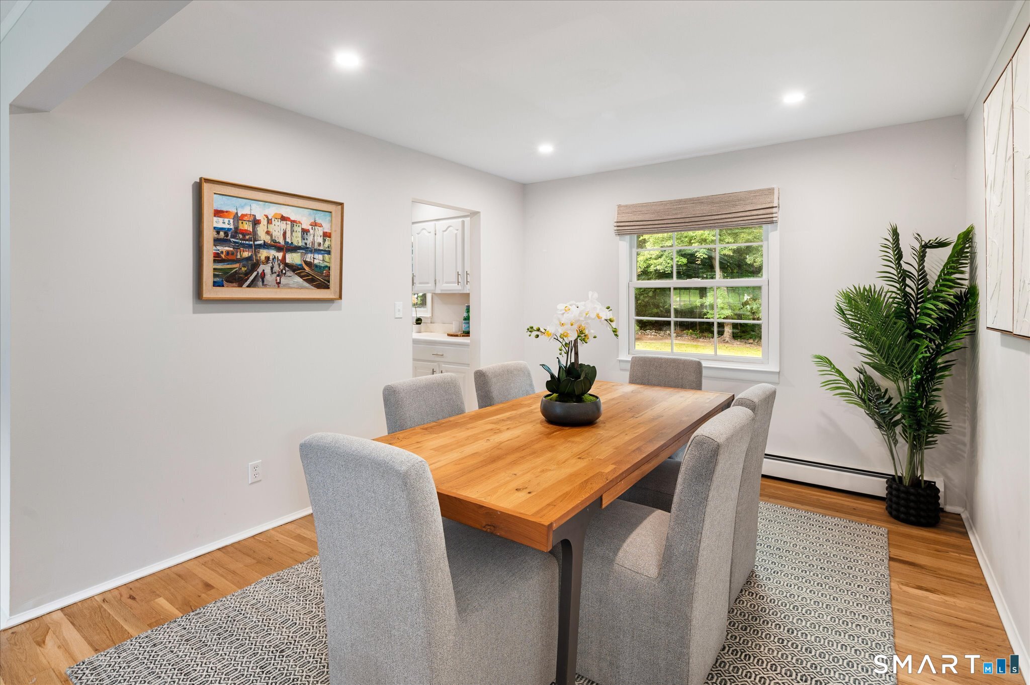 Staged dining room with a long wooden table, gray chairs, and a window overlooking greenery.