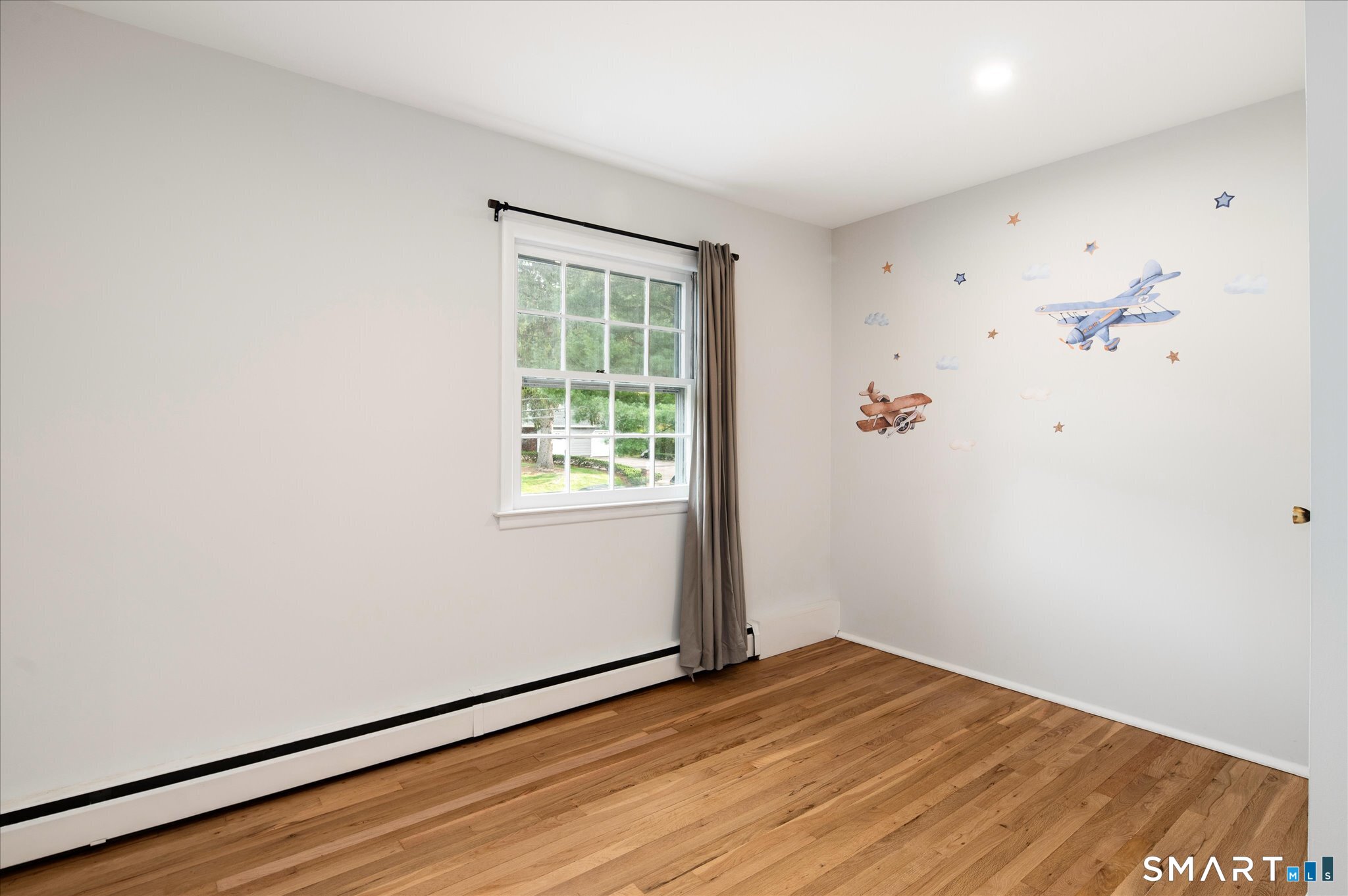 Empty bedroom with hardwood floors, a curtained window, and airplane decals on the wall.