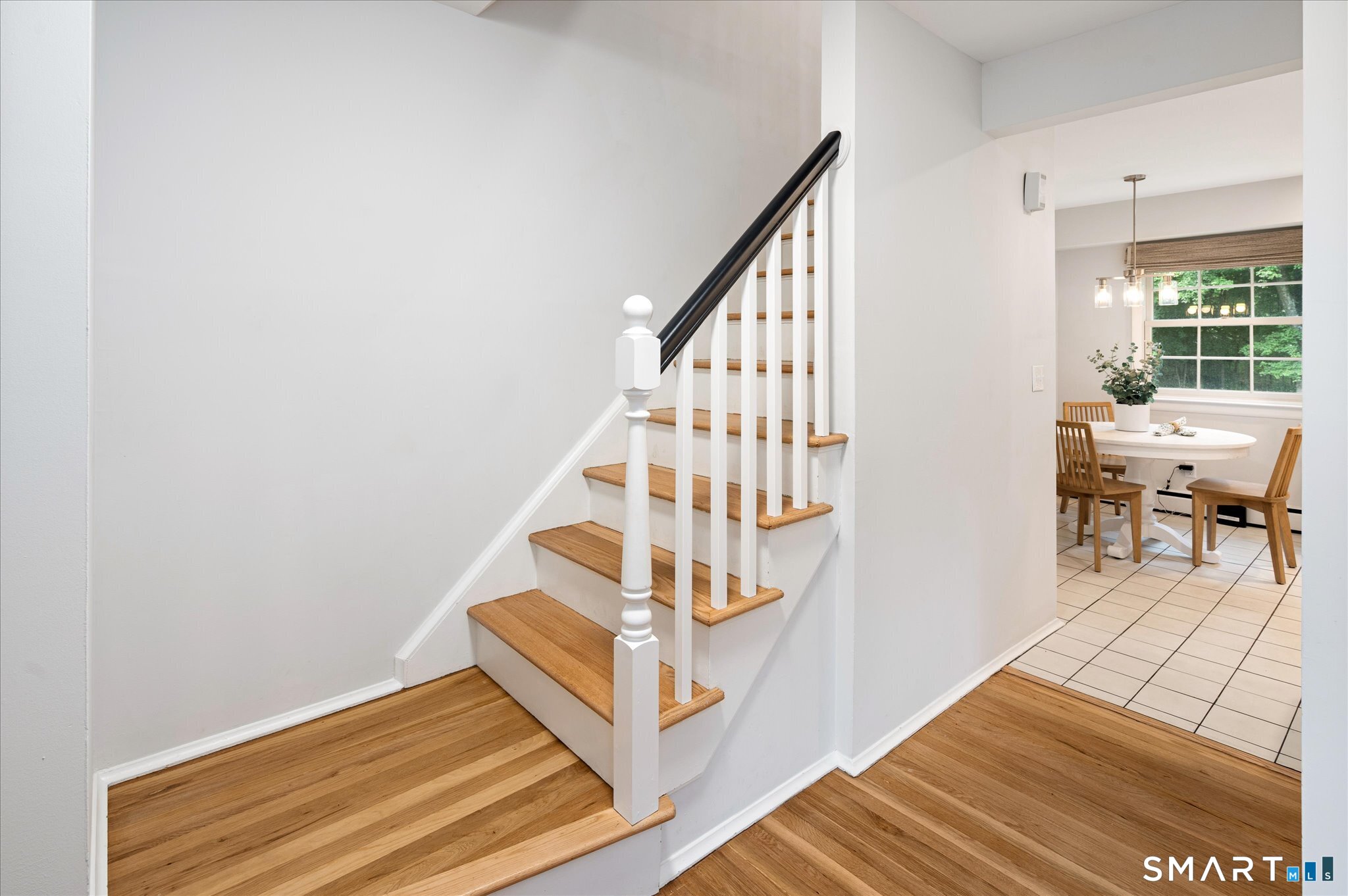 Hardwood staircase with white balusters beside a tiled dining area with a round table.