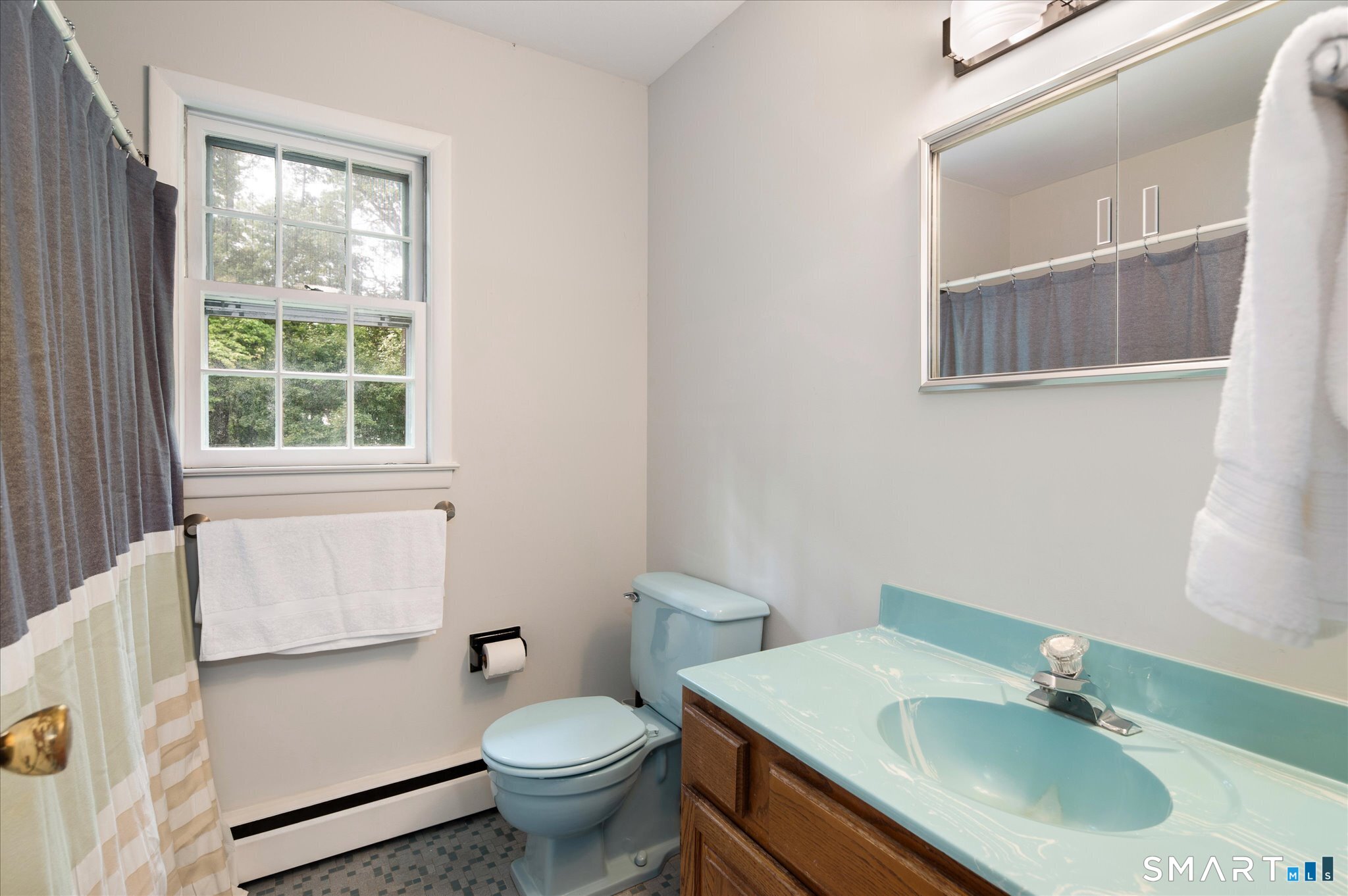 Bathroom with a turquoise sink and toilet, wood vanity, and window.