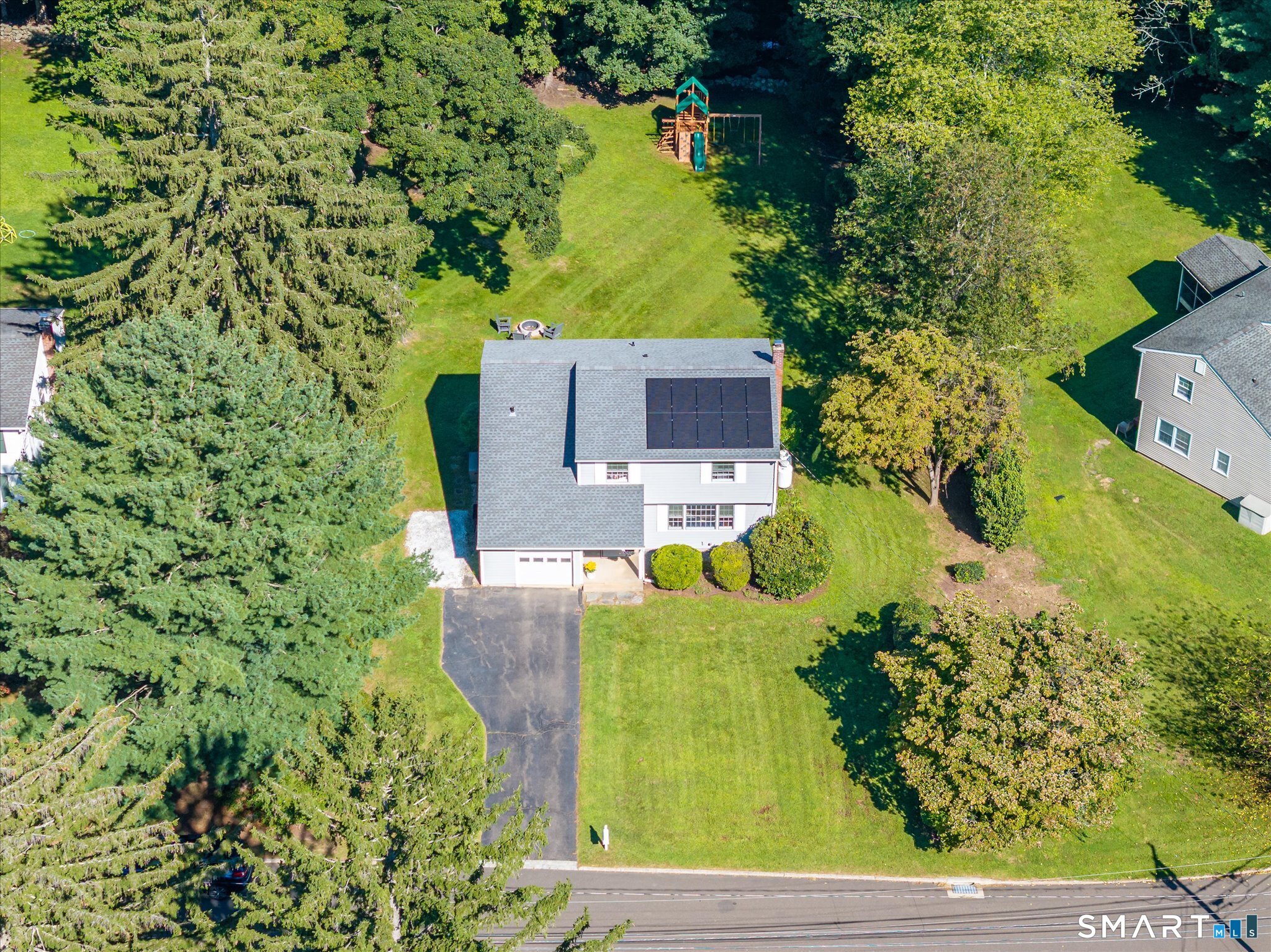 Aerial view of a two-story home with rooftop solar panels, a large lawn, and a backyard playset.