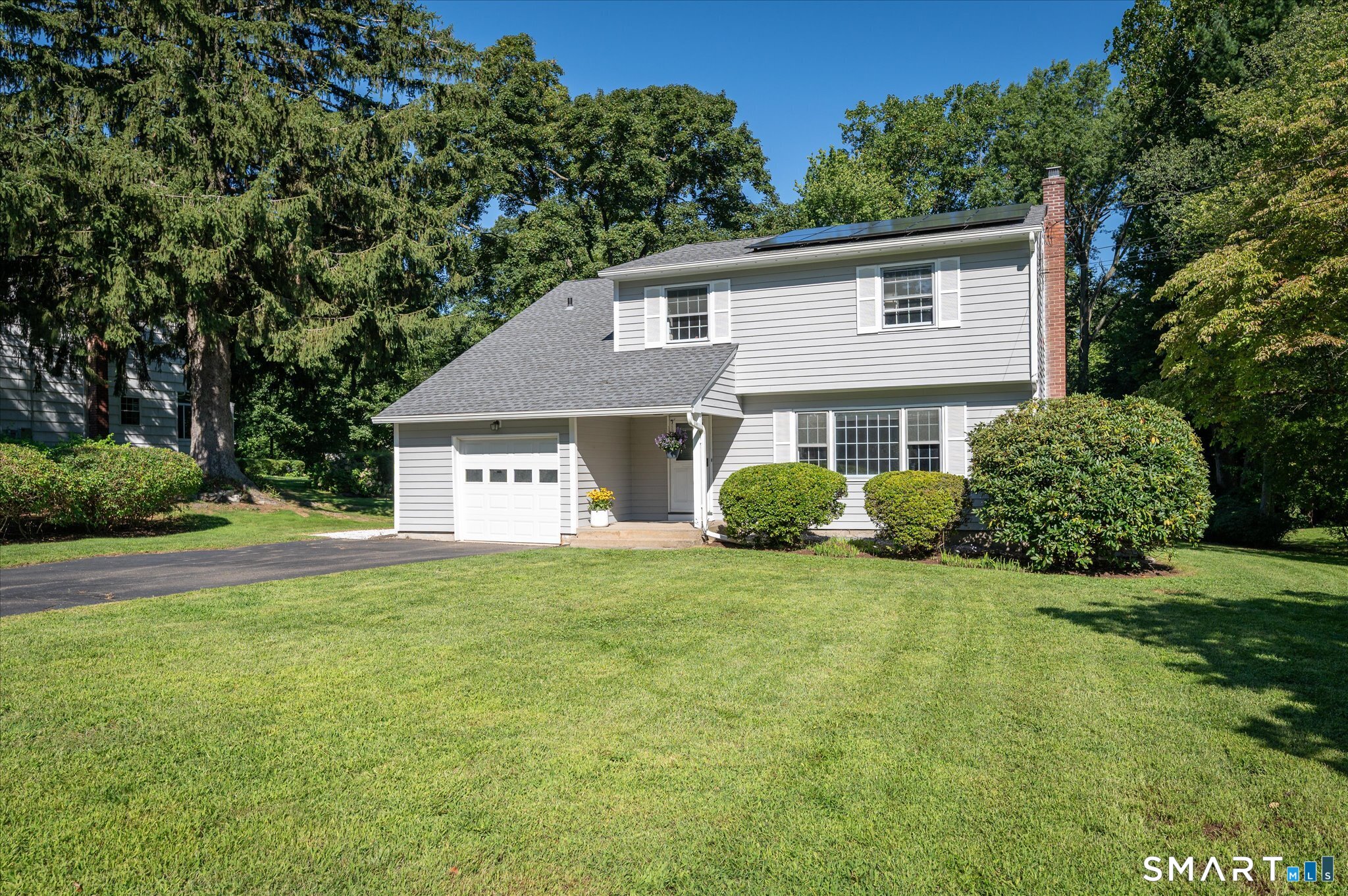 Gray two-story house with solar panels, an attached garage, and a broad green lawn.