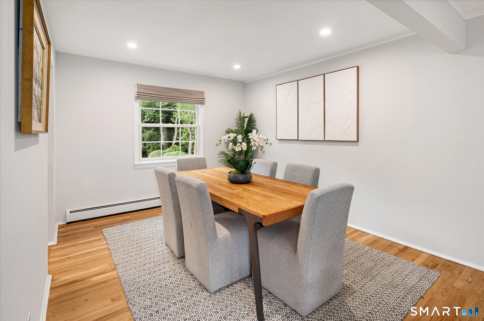 Dining room with a wood table, gray chairs, patterned rug, and window overlooking greenery.