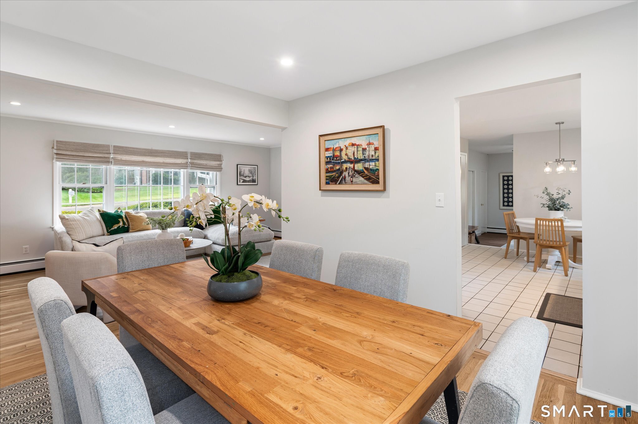 Dining table and chairs in a bright open-plan room, with the living area and tiled dining space beyond.