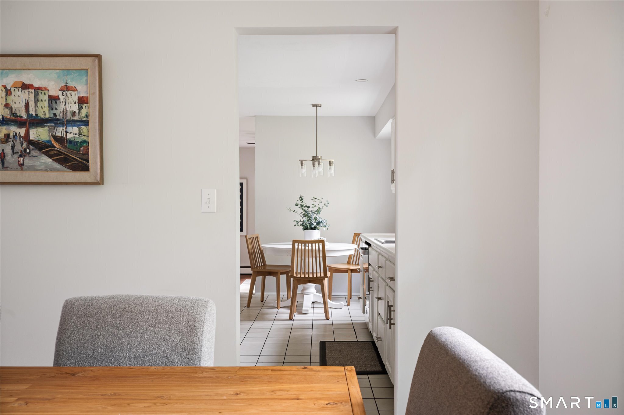 Dining nook with a round white table and wooden chairs, viewed past a wood table and kitchen cabinetry.