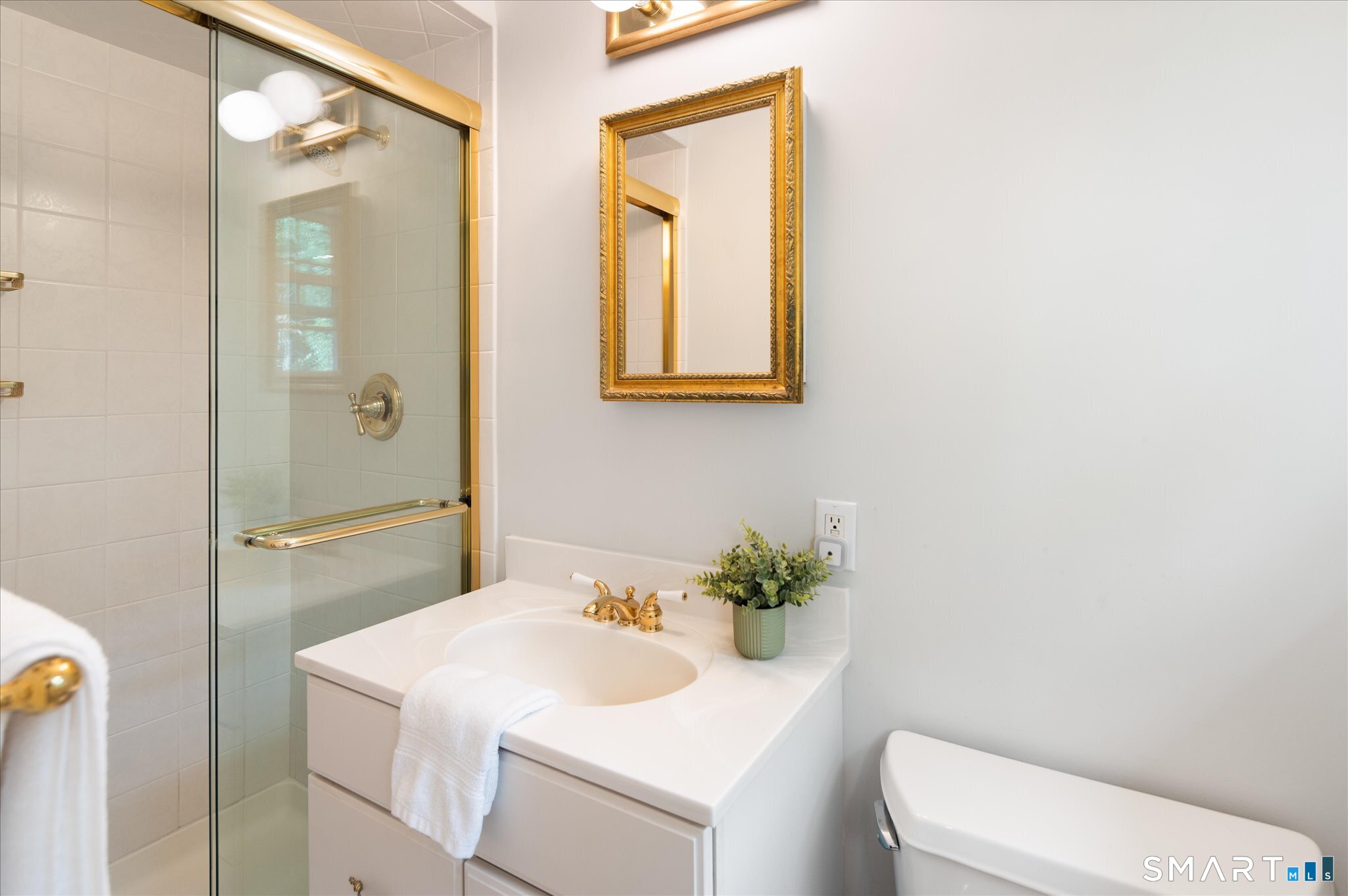 Bathroom with a glass shower, white vanity, gold fixtures, and an ornate framed mirror.