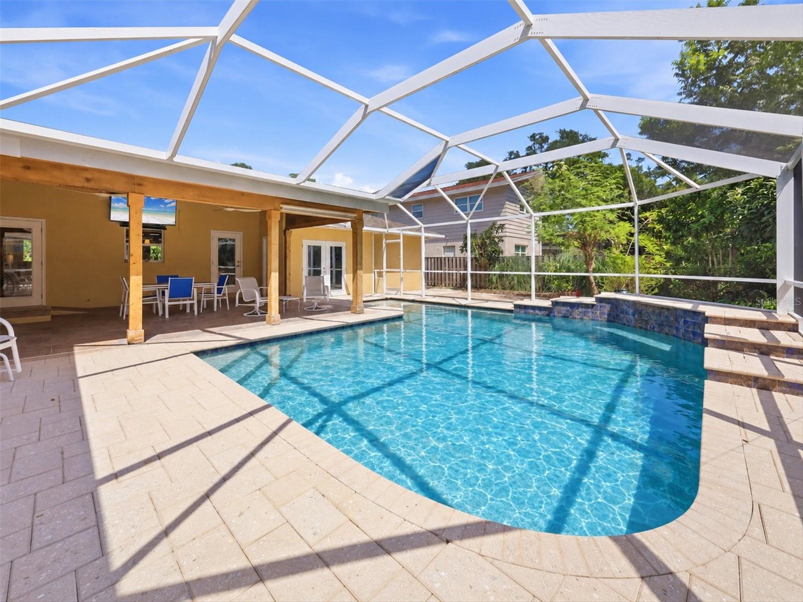 Swimming pool beneath a screened enclosure, with a paver deck and covered patio.