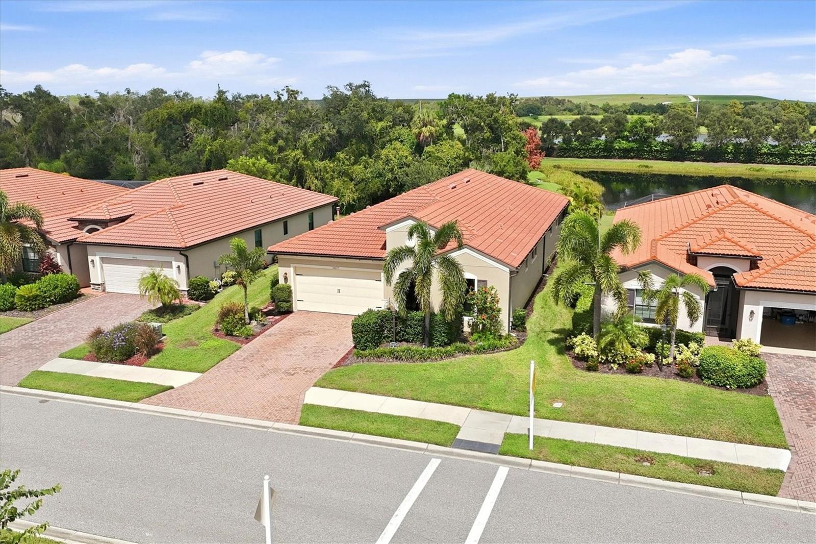 Aerial view of tile-roofed homes with palm trees, landscaped yards, and a pond behind them.