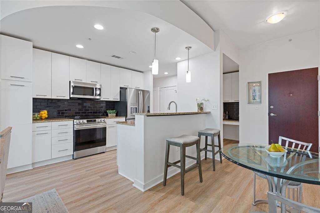 Open-plan kitchen with white cabinetry, stainless-steel appliances, black tile backsplash, and breakfast bar.