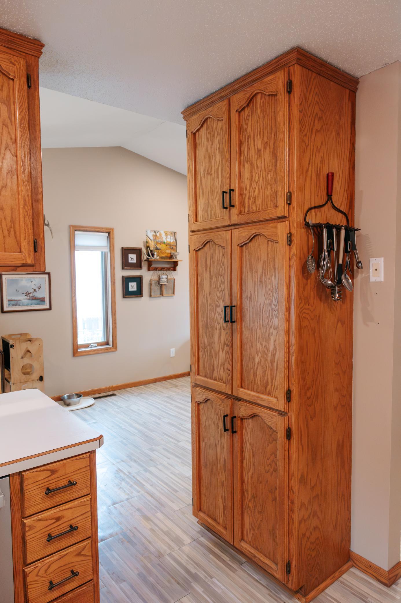 Kitchen with tall oak cabinets, black handles, pale flooring, and a wall-mounted utensil rack.