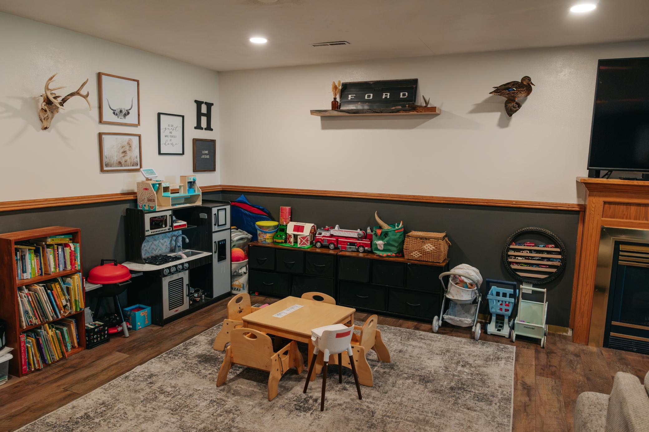 Children’s playroom with a toy kitchen, low table and chairs, bookshelves, and black storage cabinets.