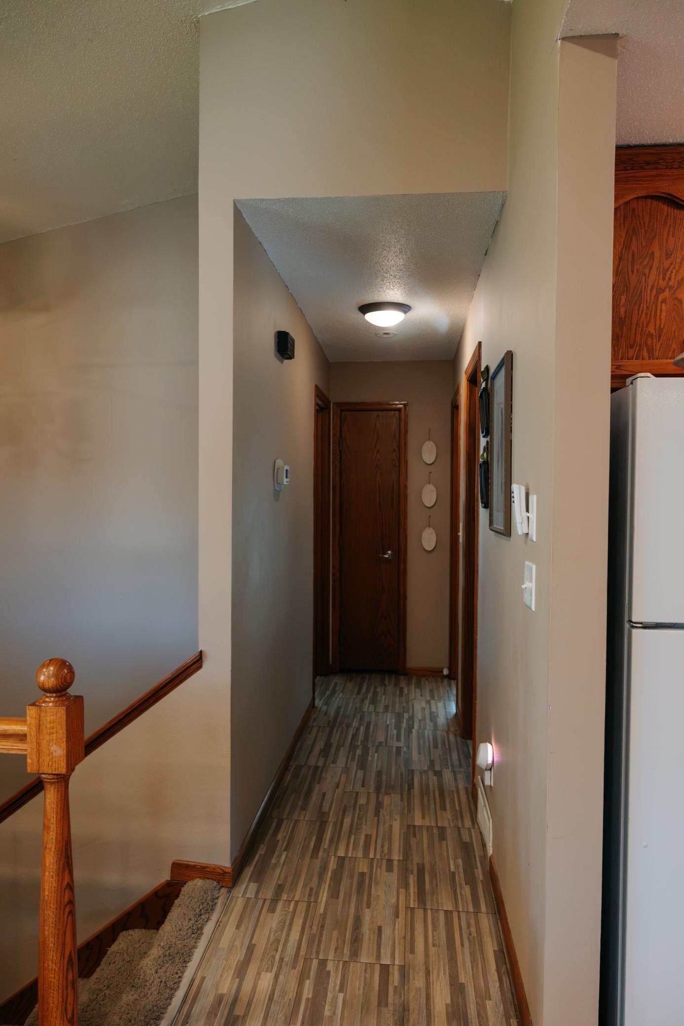 Hallway with wood-look flooring, wood trim, and a staircase banister.