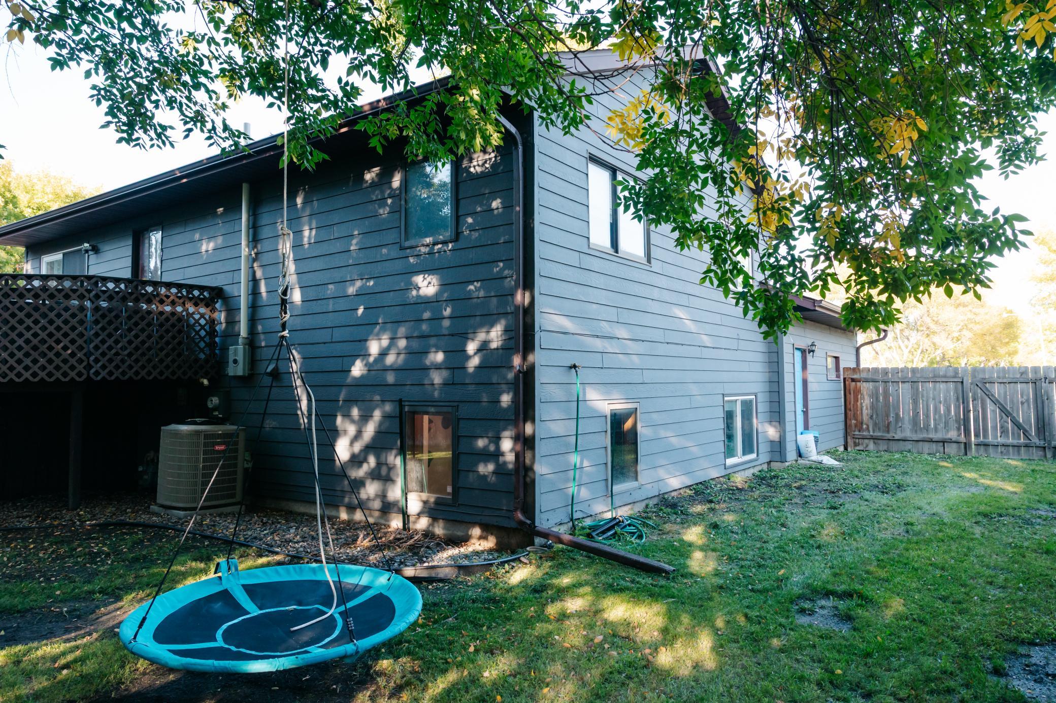 Blue-gray home exterior with a raised deck, fenced backyard, and suspended round swing.