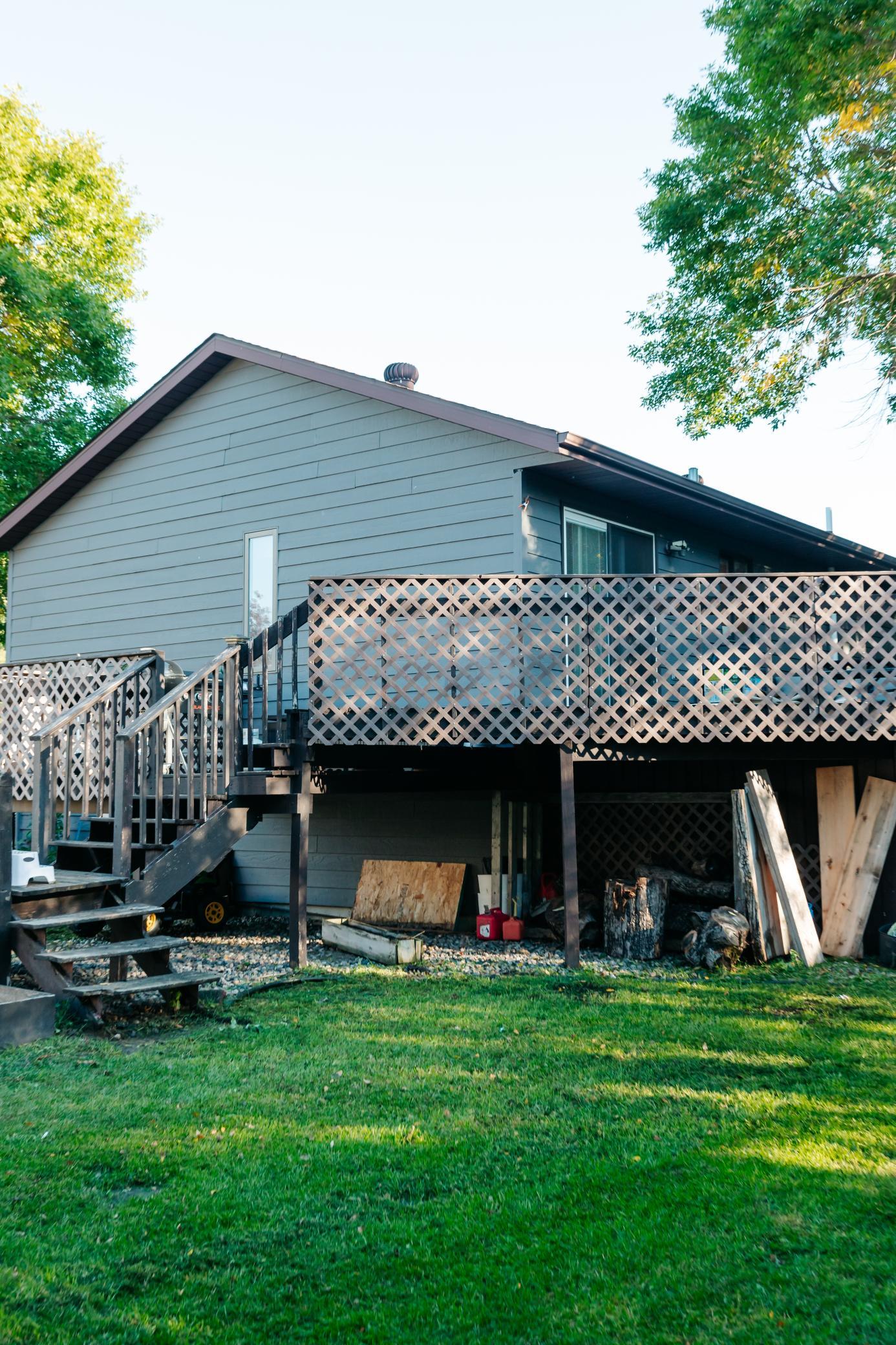 Gray-sided house with a raised lattice-enclosed deck, exterior stairs, and a grassy backyard.