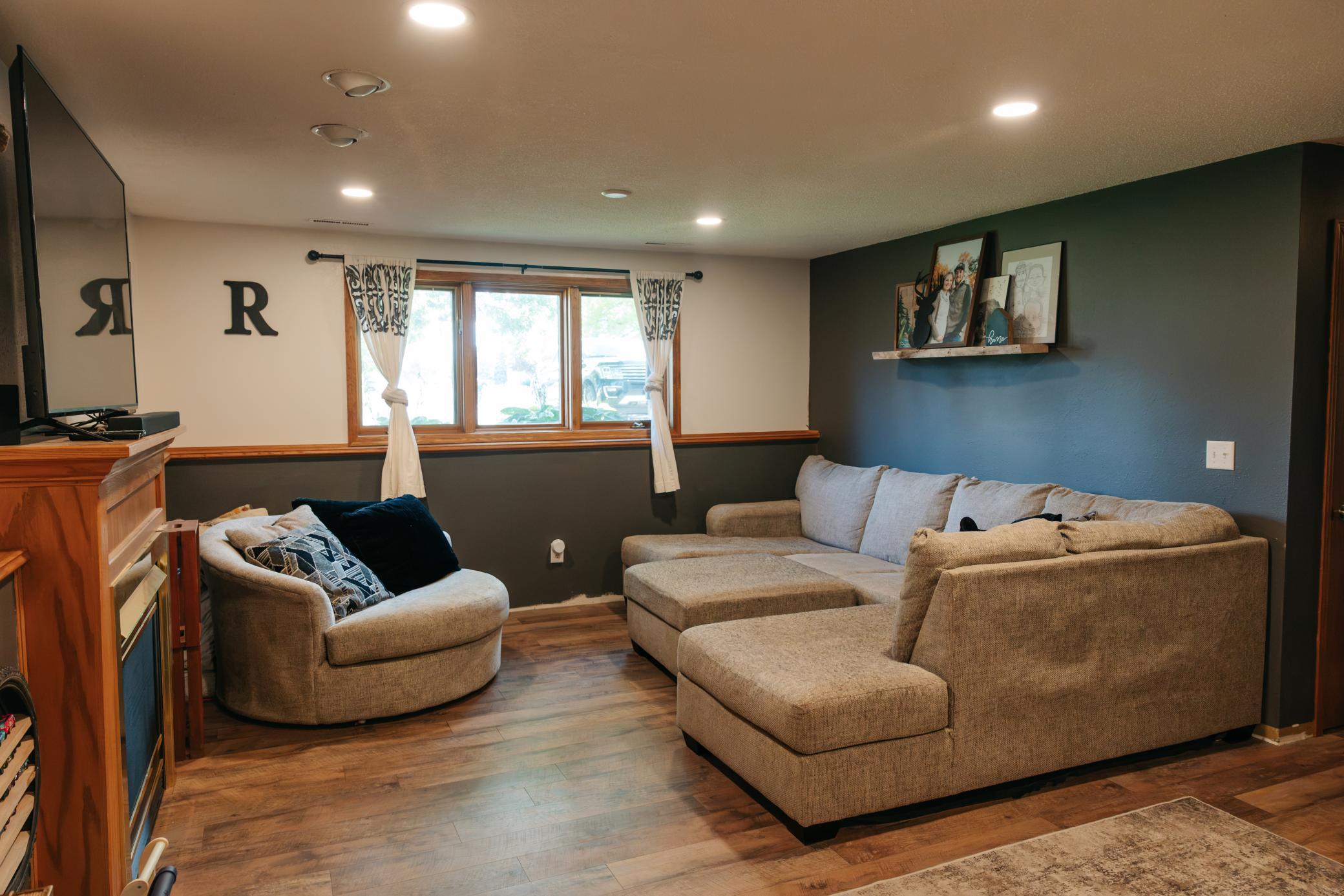 Living room with a beige sectional, matching chair, wood-look floors, and a dark blue accent wall.