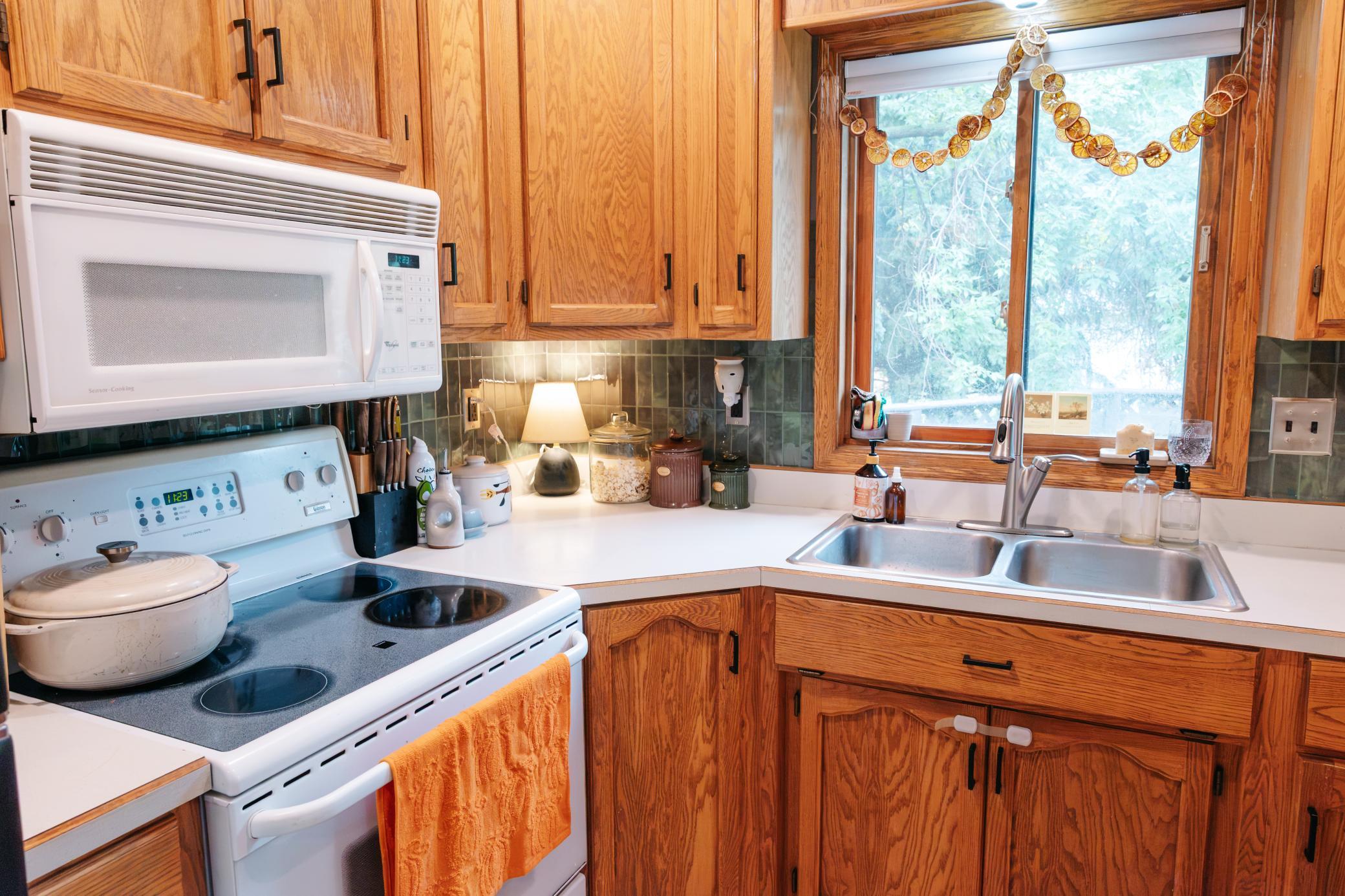 Kitchen with warm wood cabinets, a white stove, and a double sink beneath a window overlooking snow.