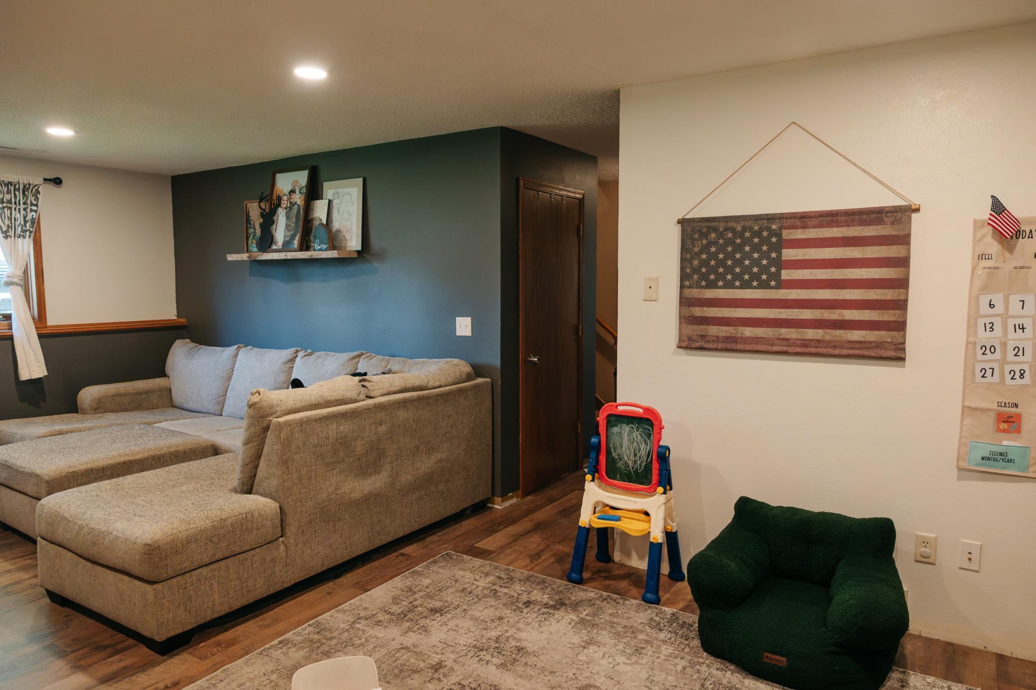 Living room with a beige sectional, dark green accent wall, and children’s easel.