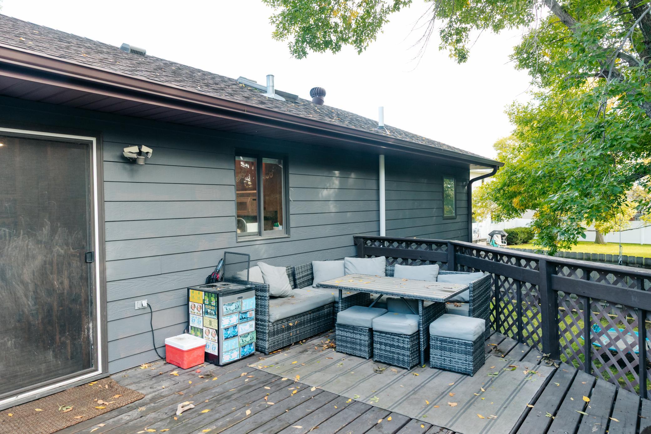 Outdoor deck with wicker sectional seating and dining table beside a gray-sided home.