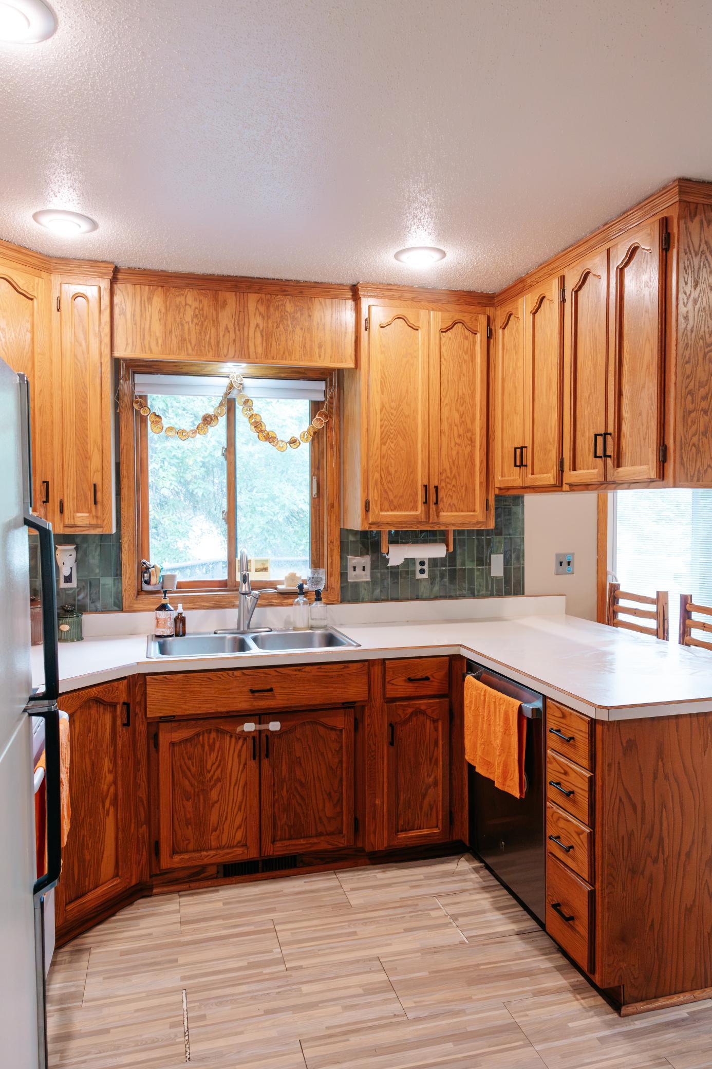 Kitchen with warm wood cabinets, green tile backsplash, and a double sink beneath the window.