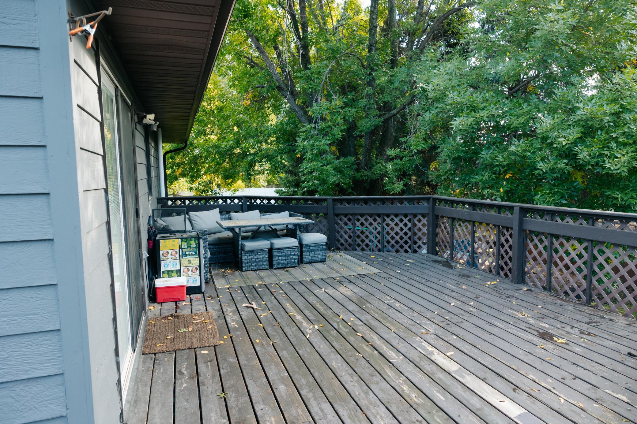 Spacious wood deck with cushioned seating and leafy trees beyond the lattice railing.