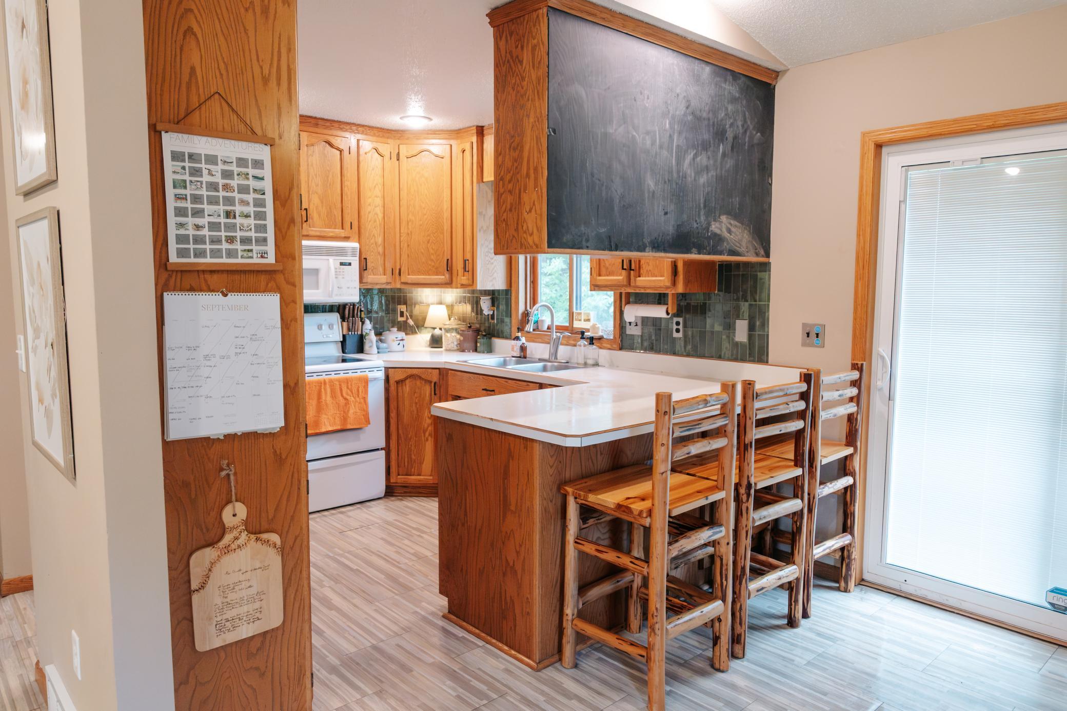 Kitchen with warm wood cabinets, a white island, rustic bar stools, and a large black range hood.