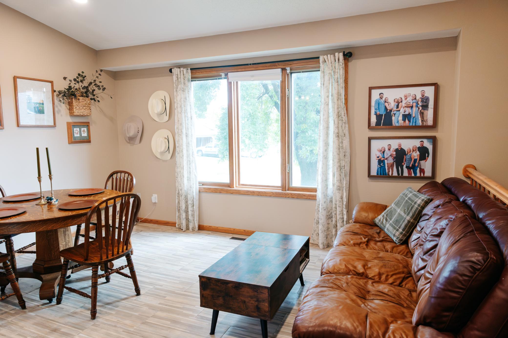 Living and dining room with a brown leather sofa and large curtained window.