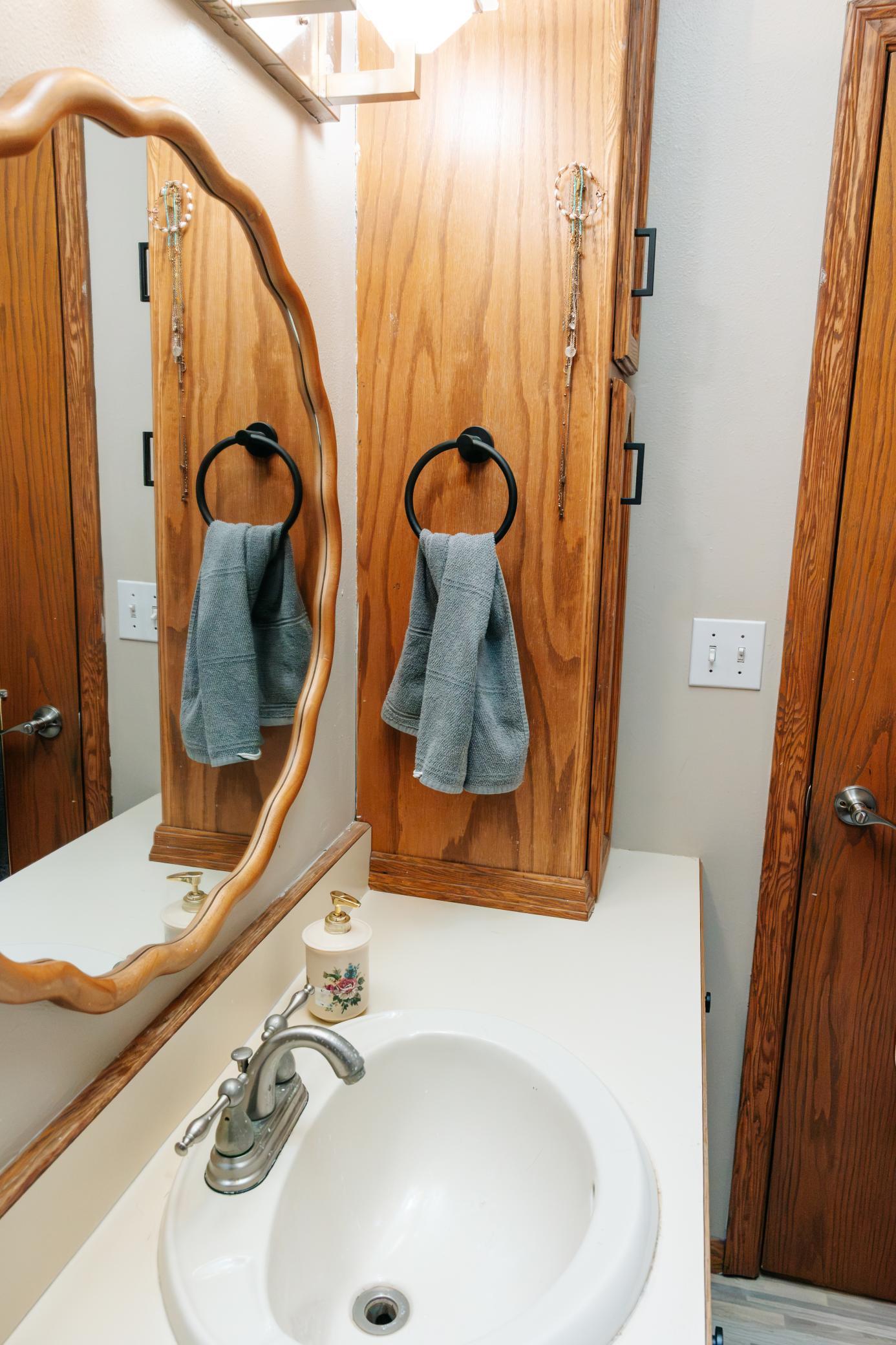 Bathroom vanity with a white sink, ornate wood mirror, and gray towel.
