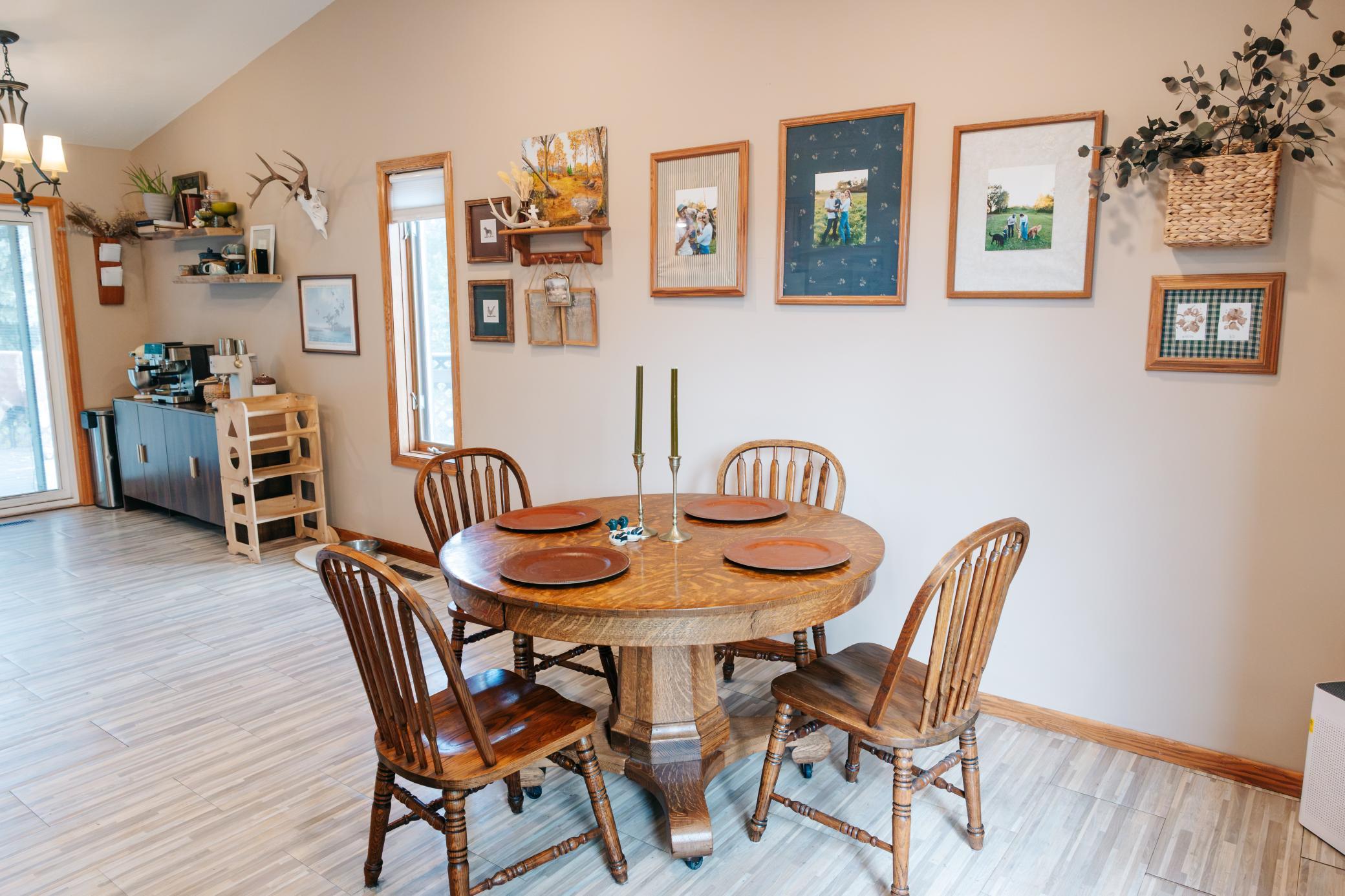Dining room with a round wooden table, four chairs, and framed photos covering the wall.