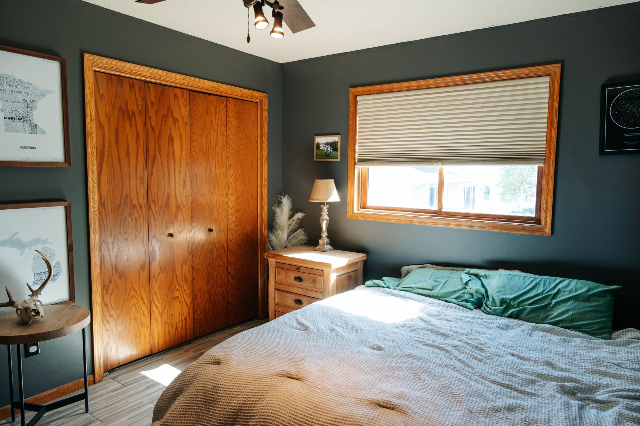 Bedroom with a wood-paneled sliding closet, dark green walls, and a sunlit window above the bed.