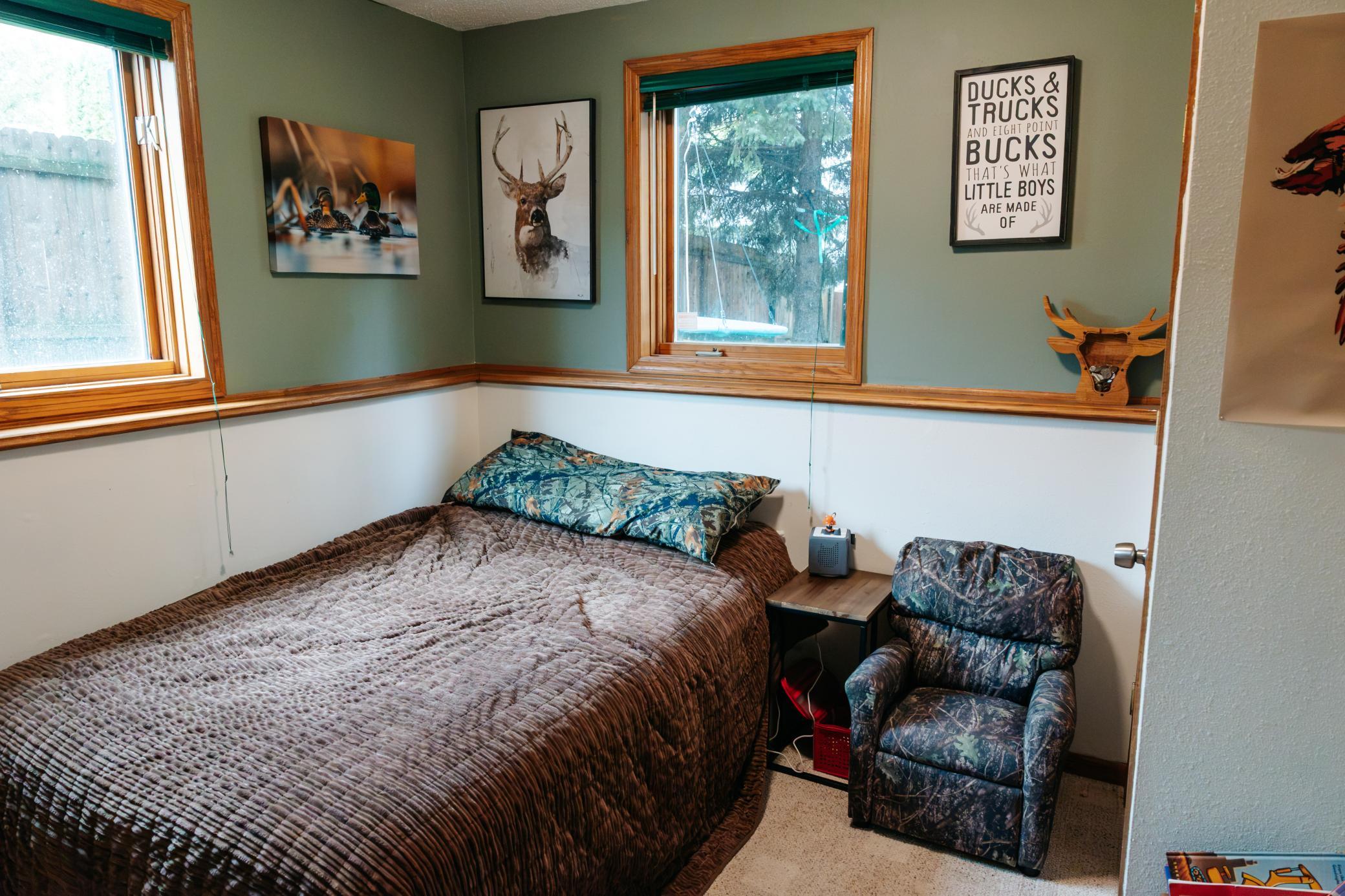 Bedroom with a large bed, camouflage recliner, wood-trimmed windows, and wildlife wall decor.